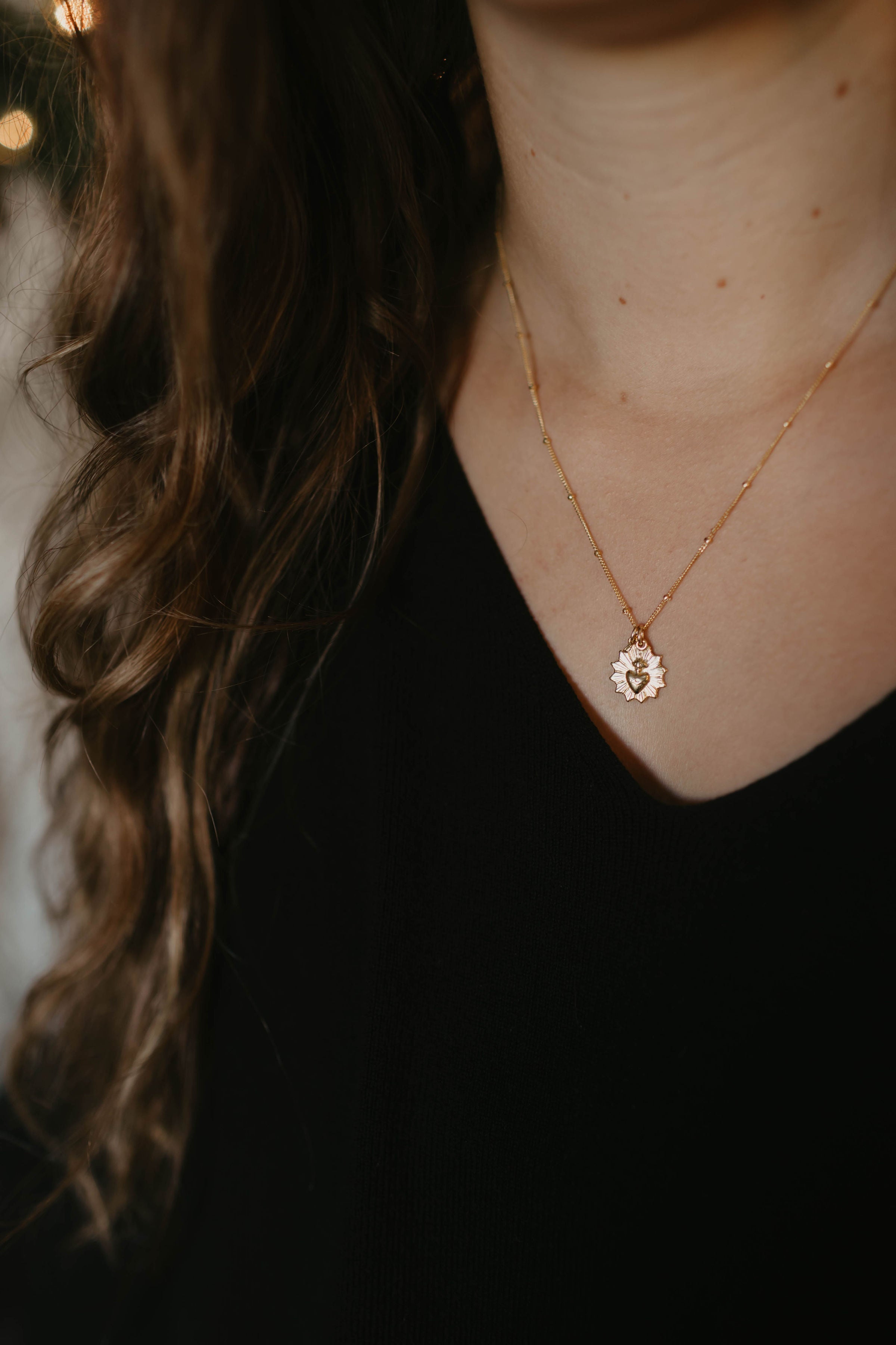 Gold-tone pendant necklace worn on neckline with small sacred heart medal charm