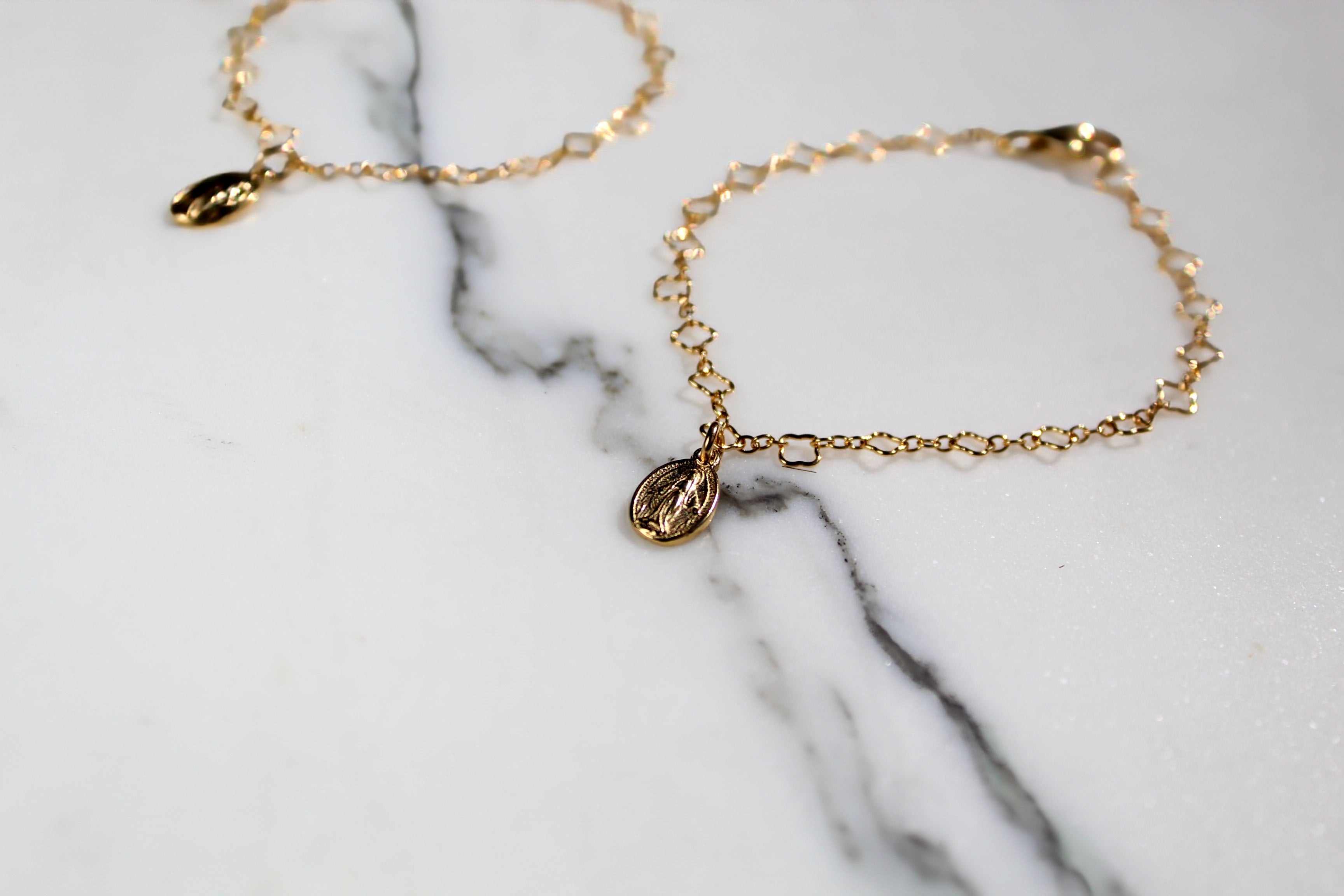 Gold-tone charm bracelet with oval medal charm on chain links, flat on marble
