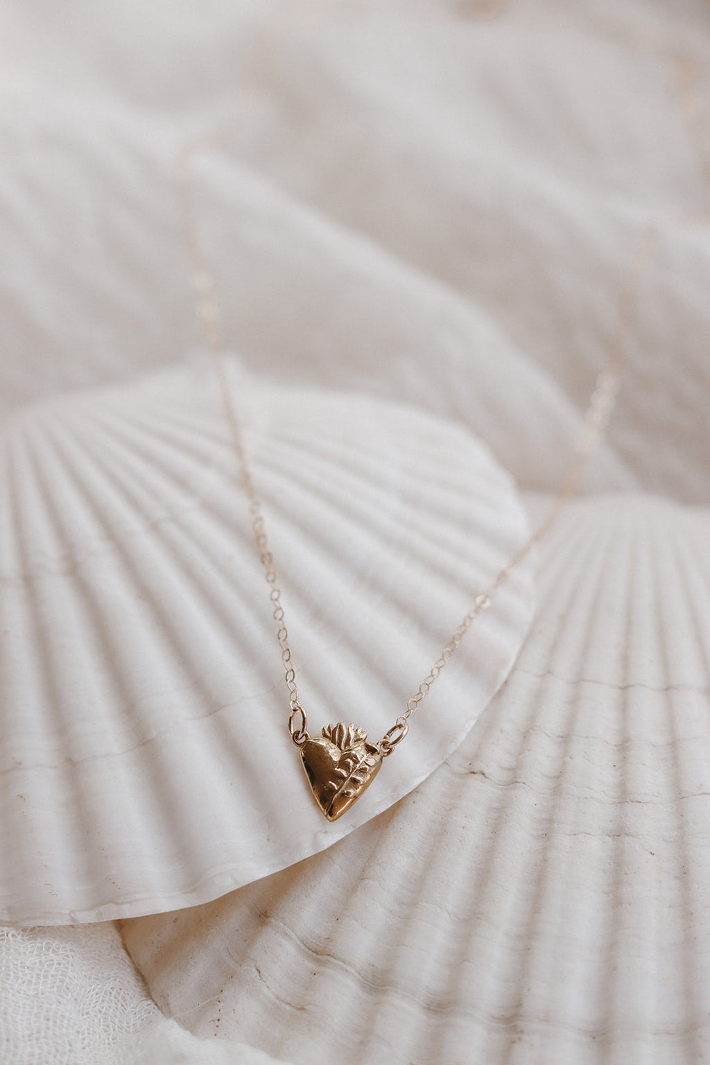 Gold-tone heart pendant necklace lying on white textured fabric