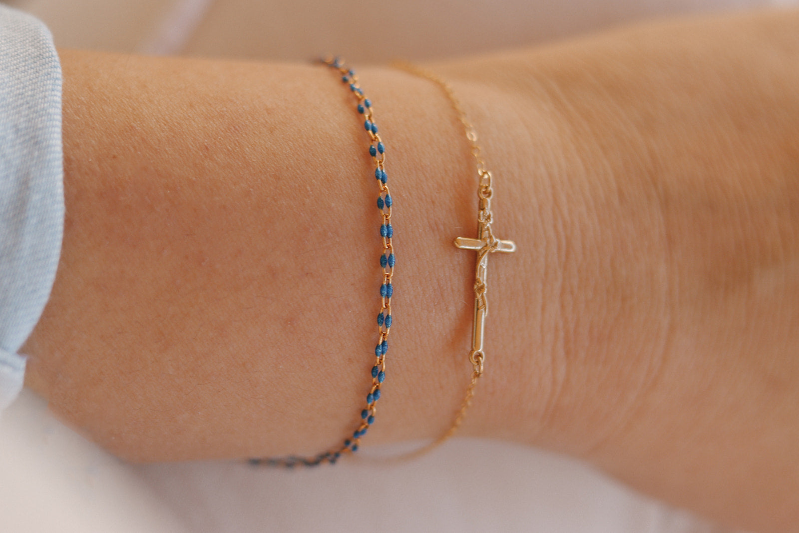 Wrist view of gold cross charm bracelet and blue beaded bracelet bands