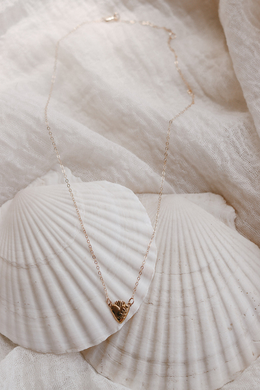 Gold-tone heart pendant necklace draped on white shell-like fabric