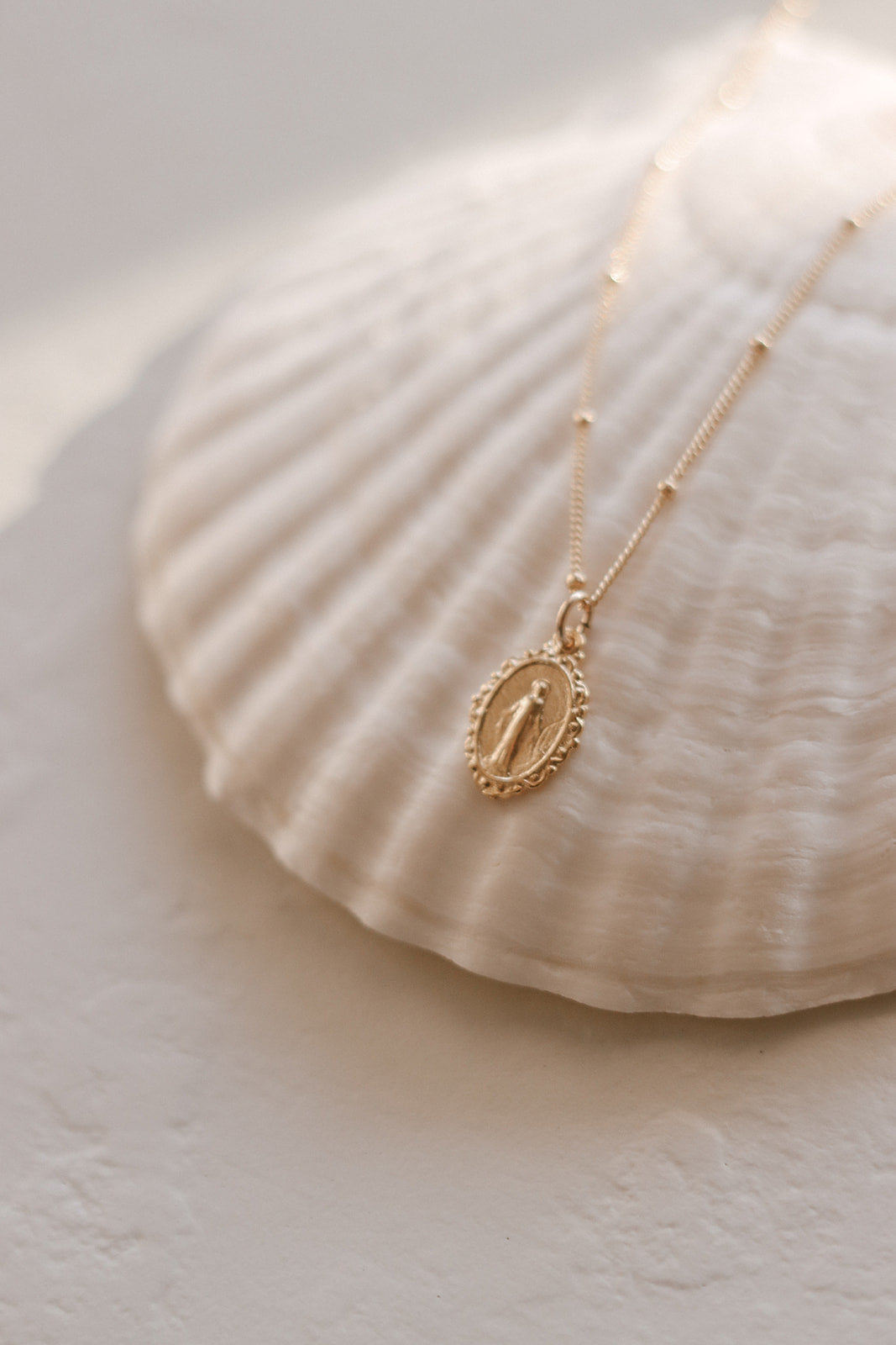 Gold-tone oval medal necklace with fine chain over white shell detail