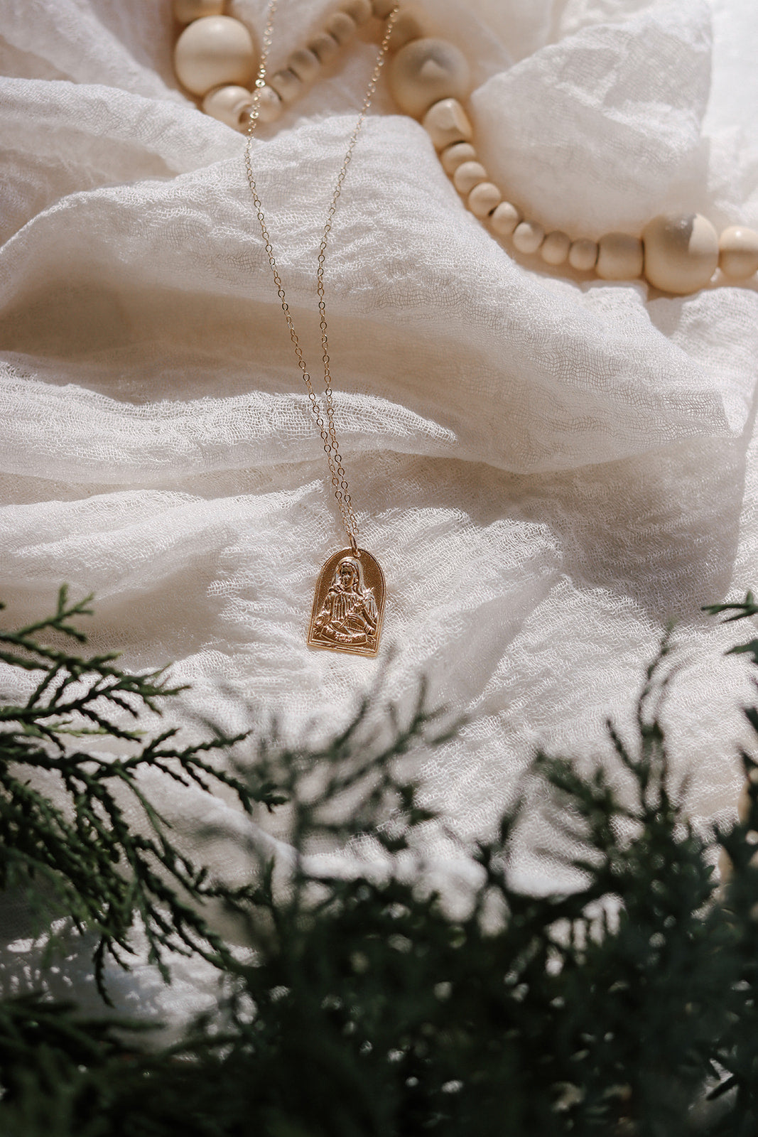 Gold-tone St. Catherine pendant on long chain, shown with bead strands