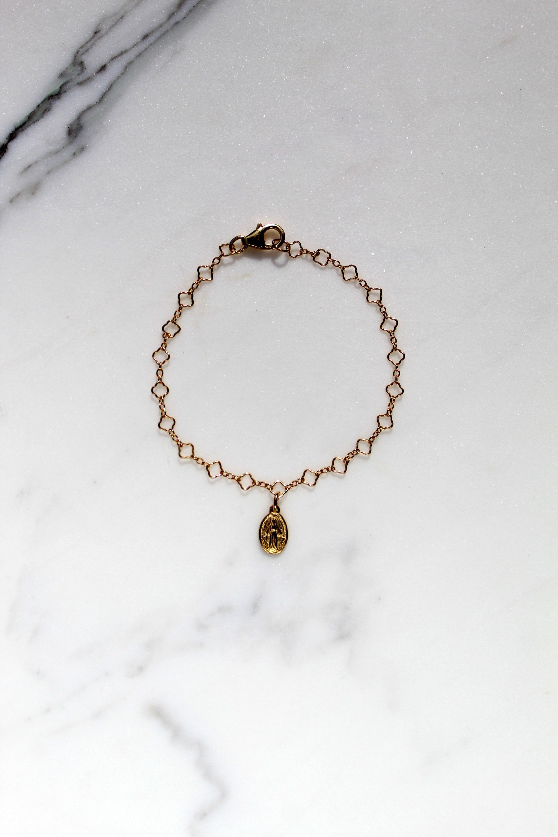 Gold children’s bracelet with oval medal charm on a flat marble surface.