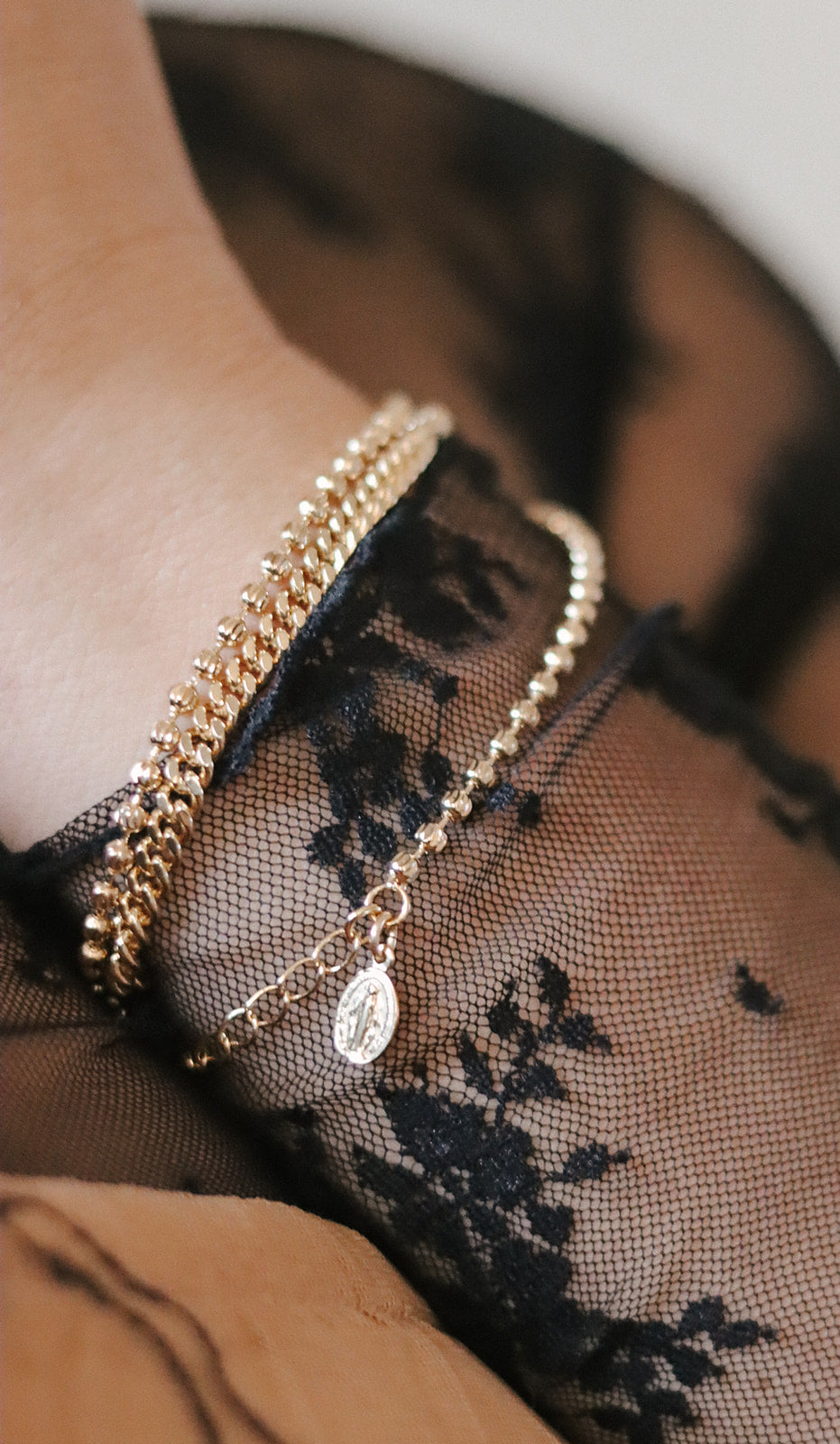 Gold-tone medal charm bracelet layered on wrist with oval pendant