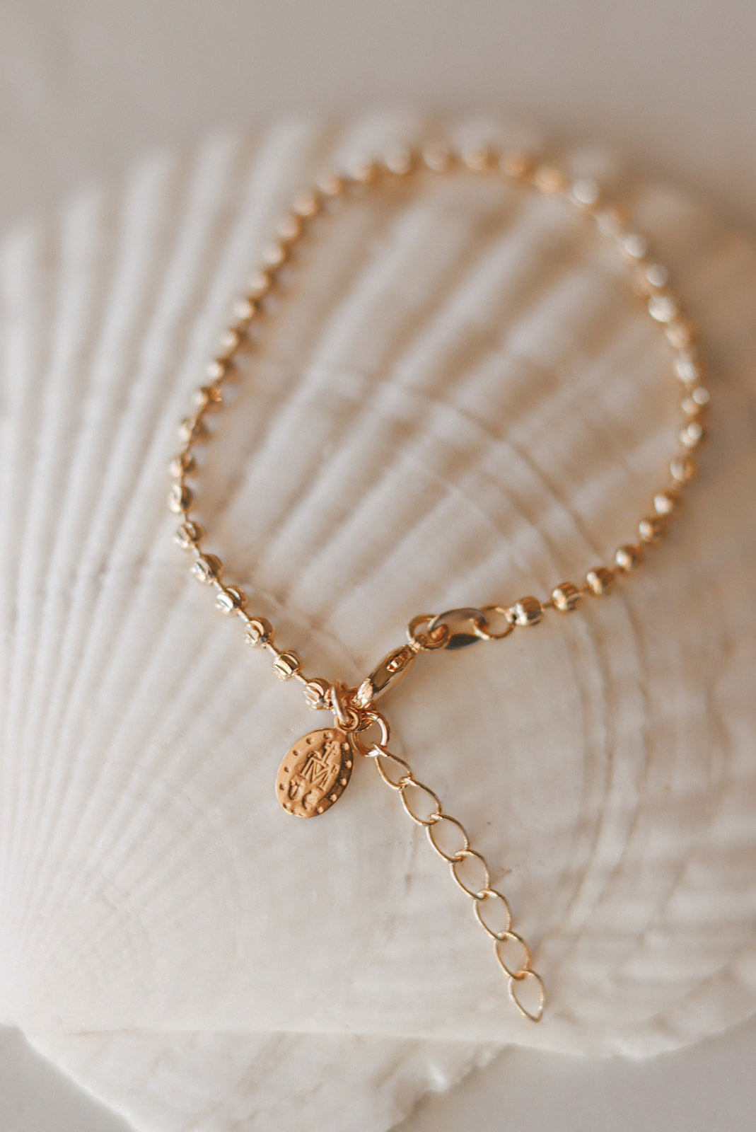 Gold-tone medal bracelet detail with oval medal charm and small link chain drop.