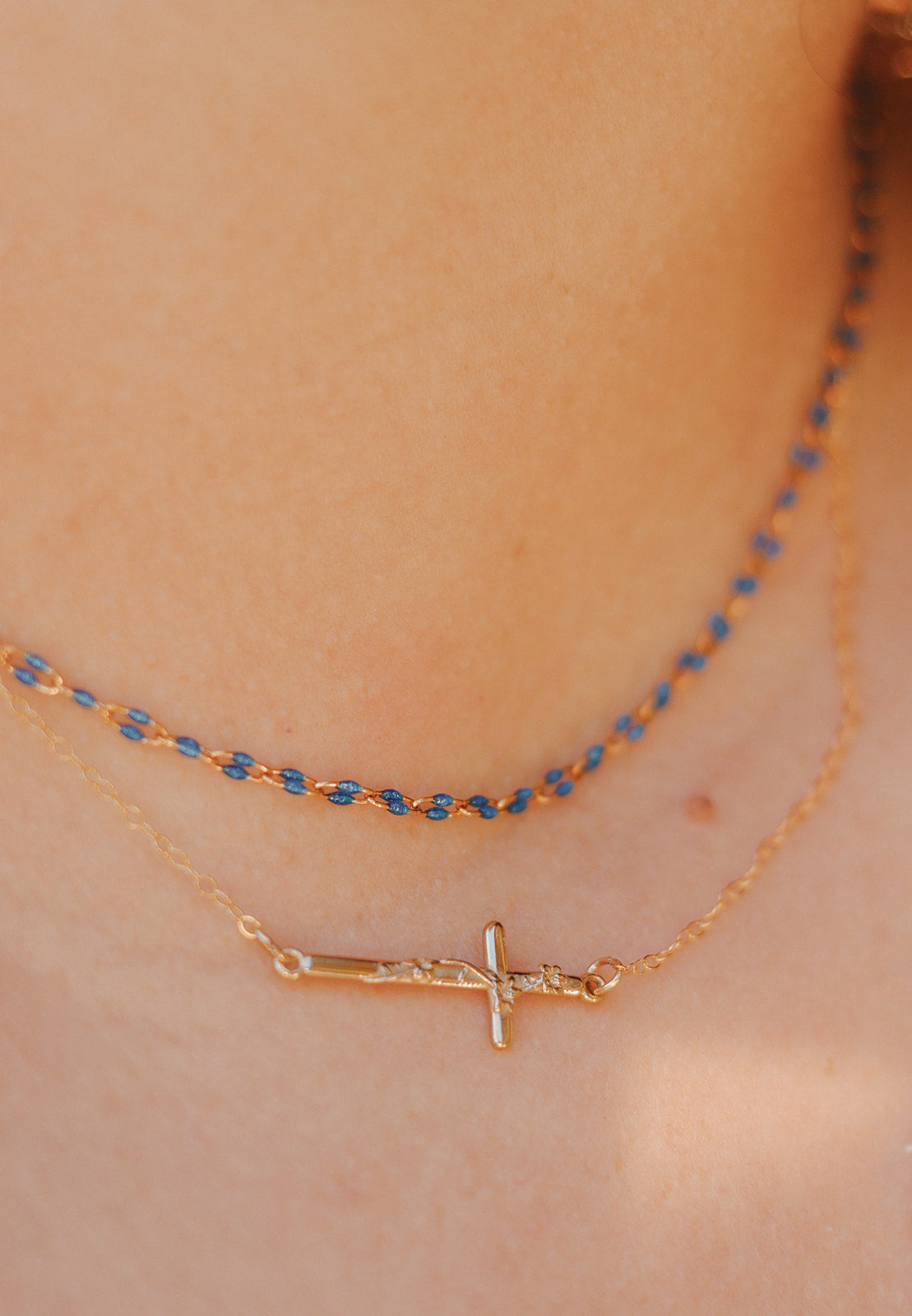 Necklace with gold-tone cross charm and a blue beaded layer chain.