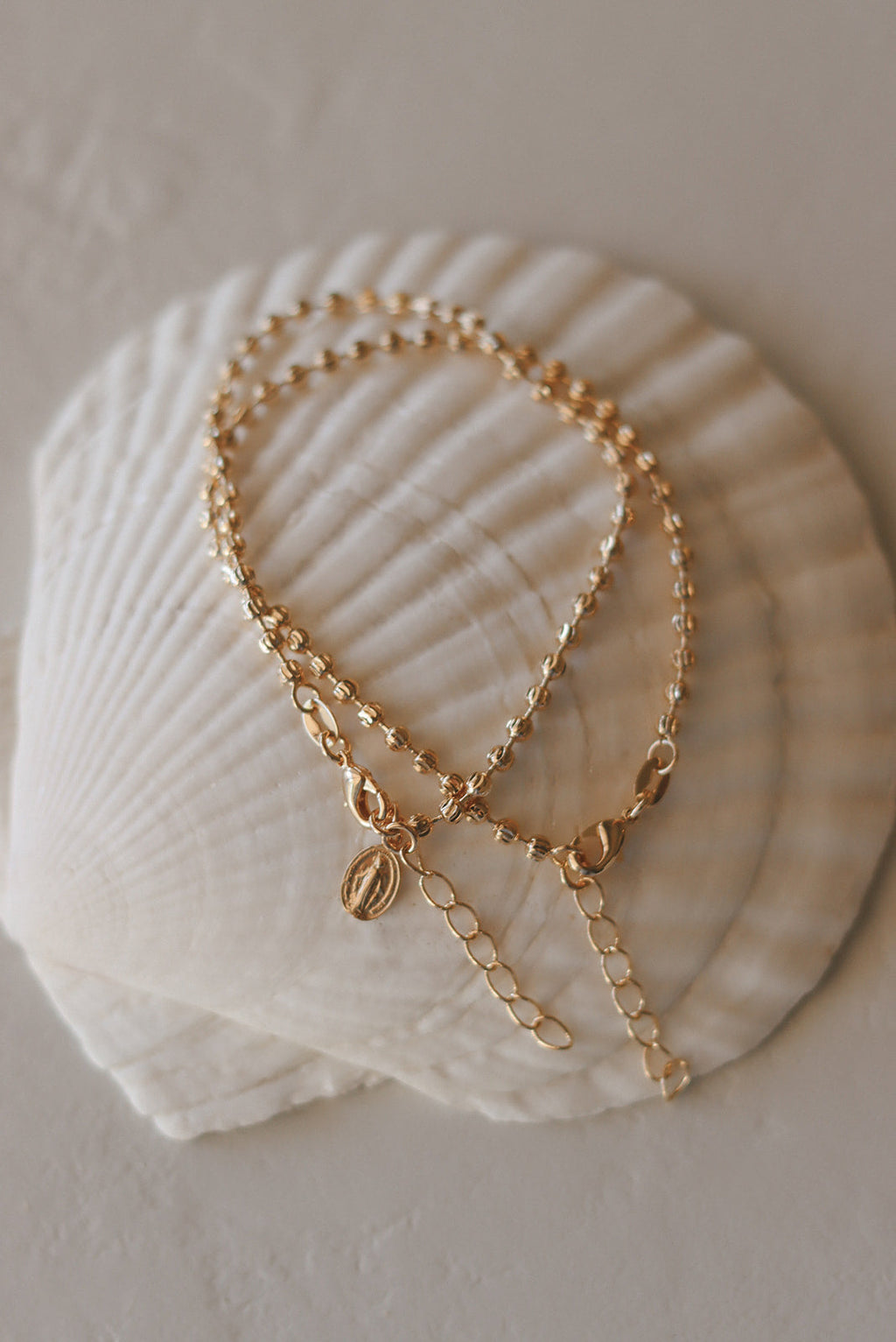 Gold-tone medal bracelet with oval charm and long dangling chain detail.