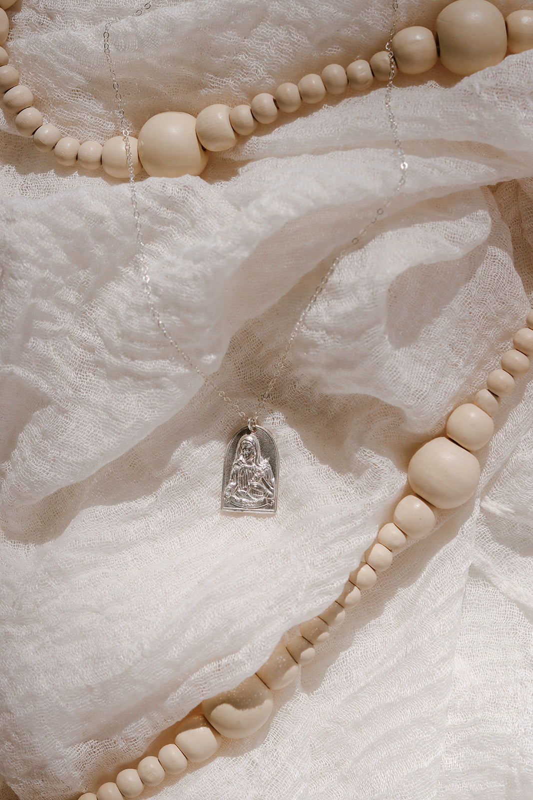 Sterling silver Saint pendant necklace resting among cream beaded strands