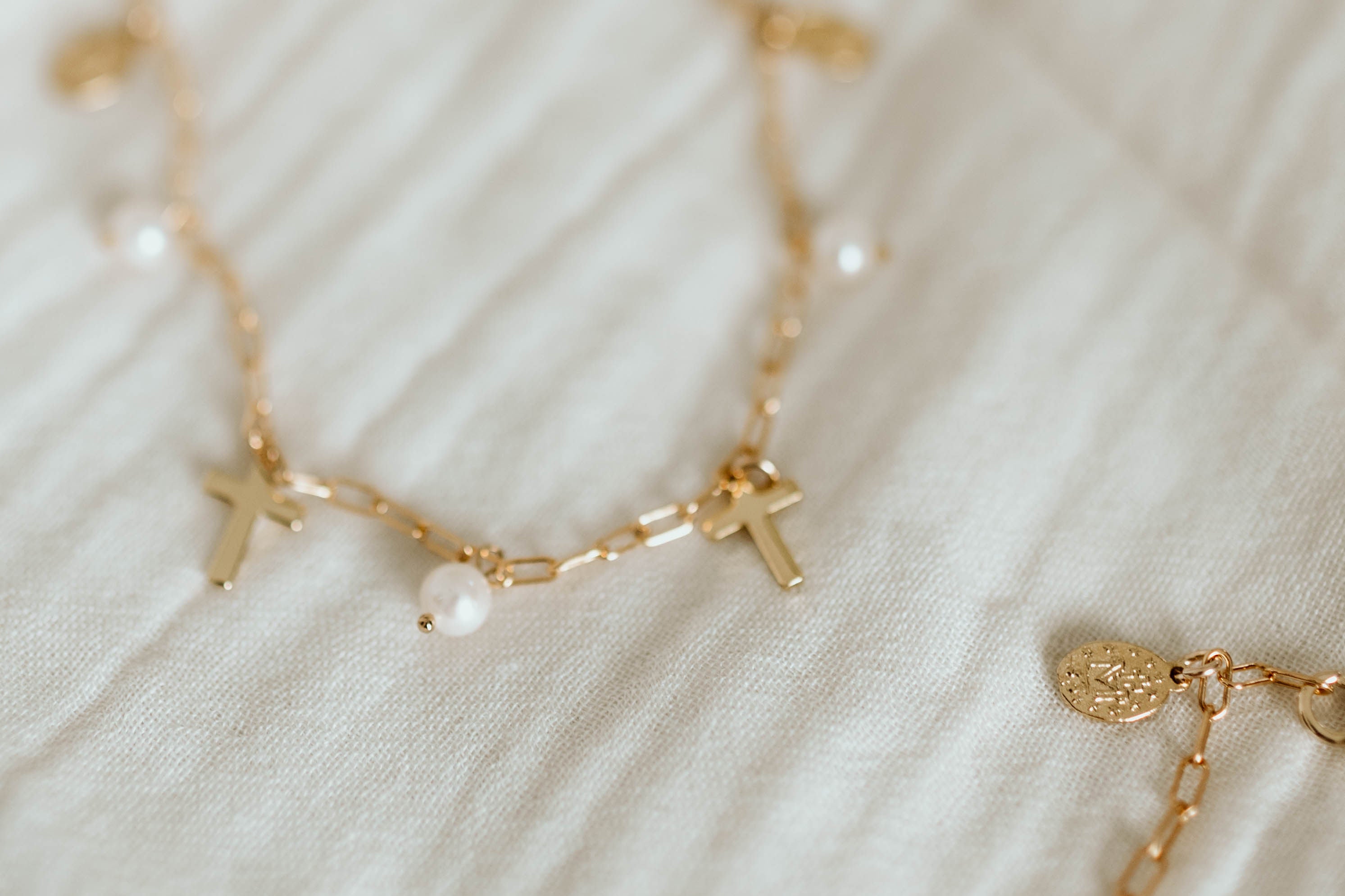 Gold-tone necklace on light fabric with cross charms and pearl center bead.