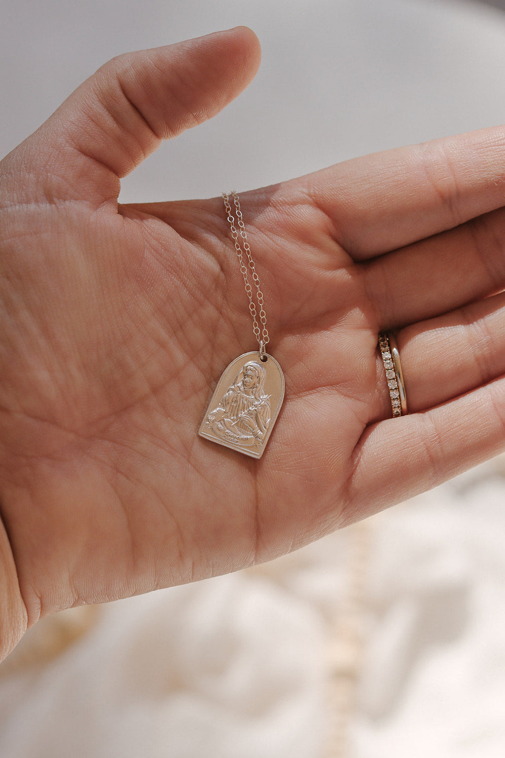 Sterling silver Saint pendant necklace shown on open palm with chain
