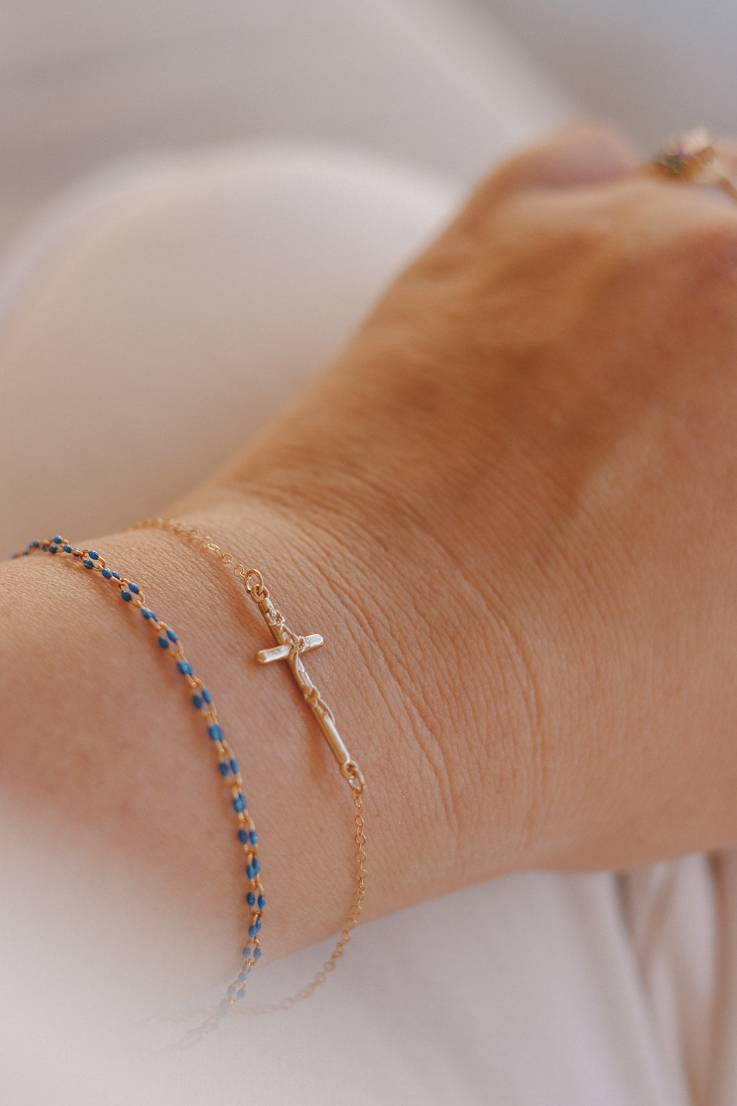 Blue beaded bracelet and gold cross charm bracelet stacked on a wrist