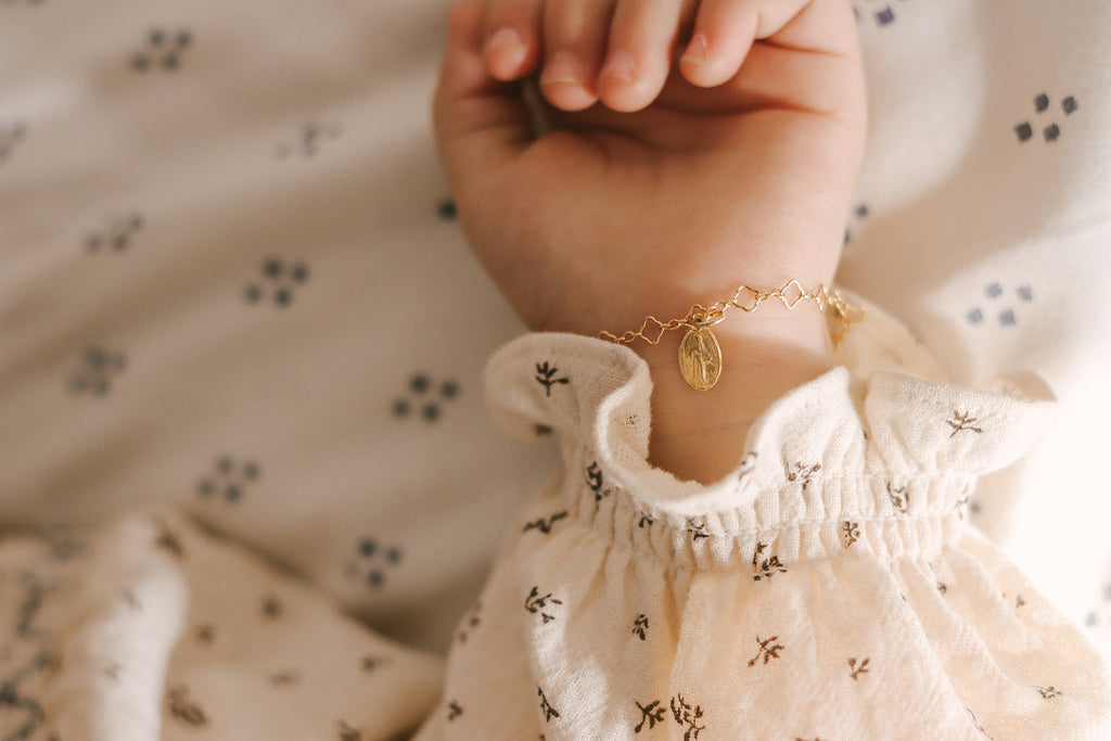 Gold children’s bracelet with oval medal charm and small chain links on wrist.