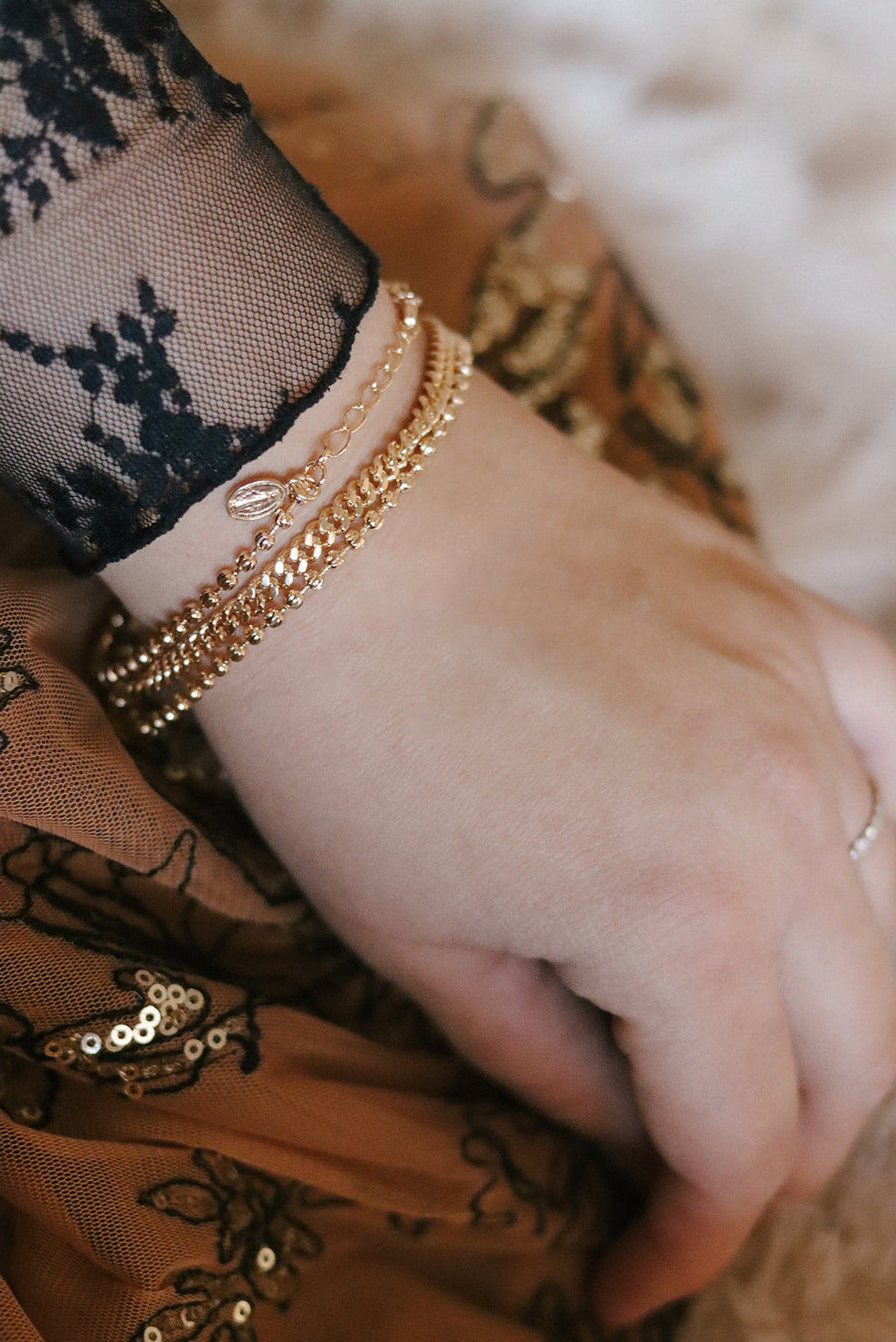 Gold-tone medal bracelet on wrist with beaded band and oval charm