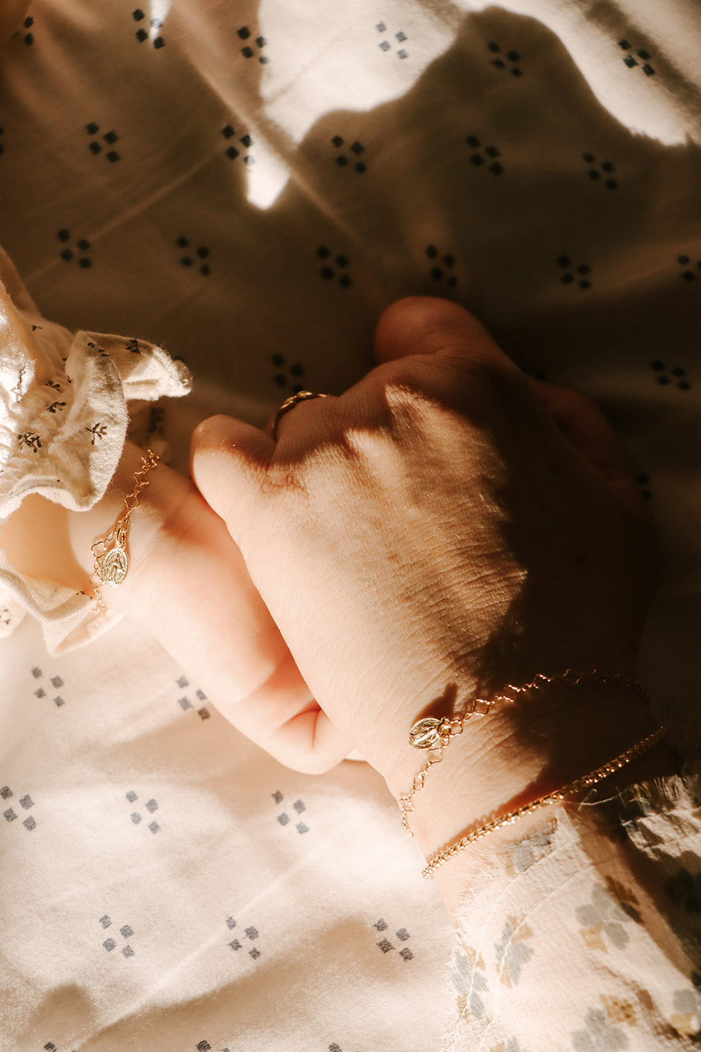 Gold-tone charm bracelet with oval medal charm on wrist against lace fabric