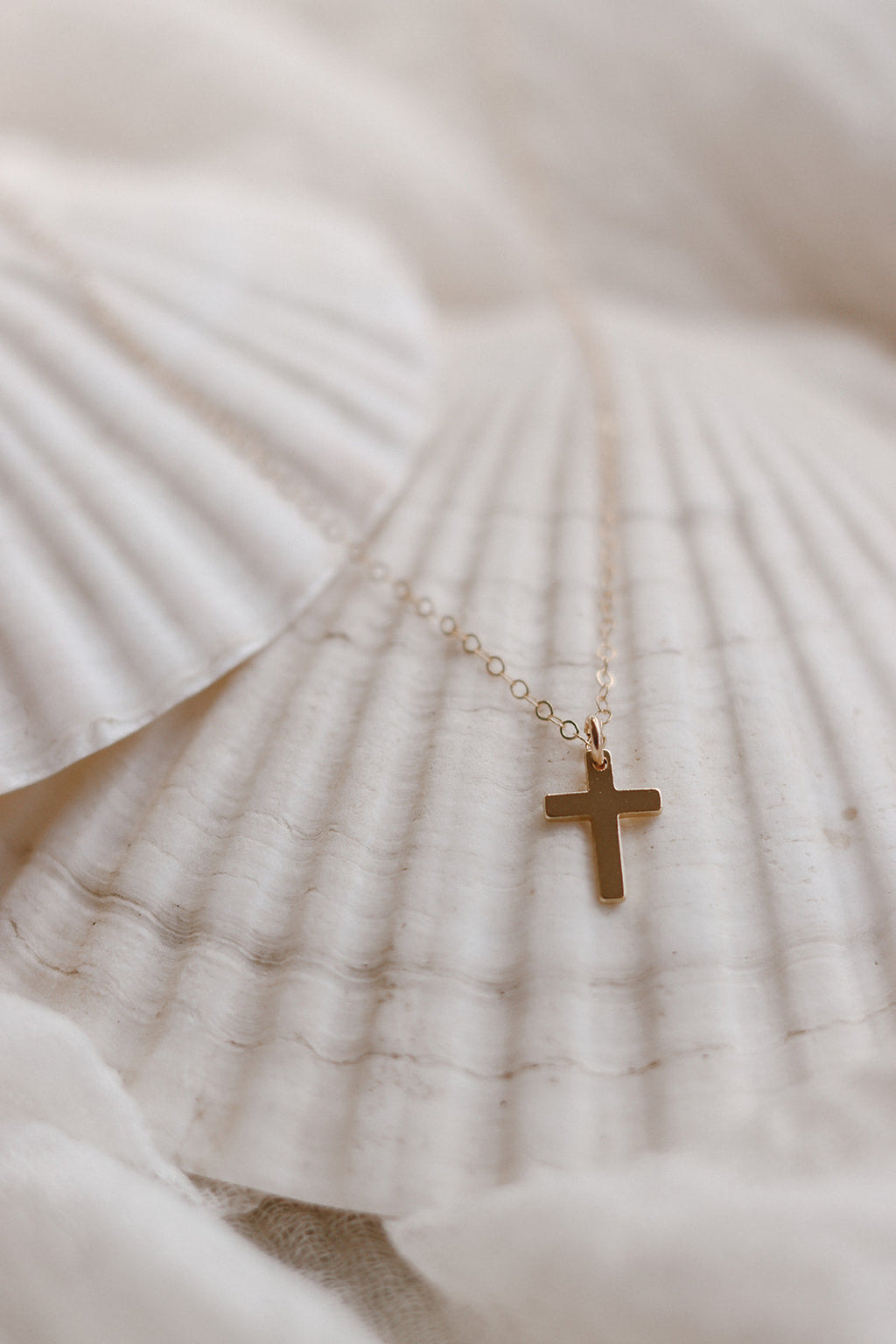 Gold cross pendant necklace on thin chain over white fabric, small cross charm
