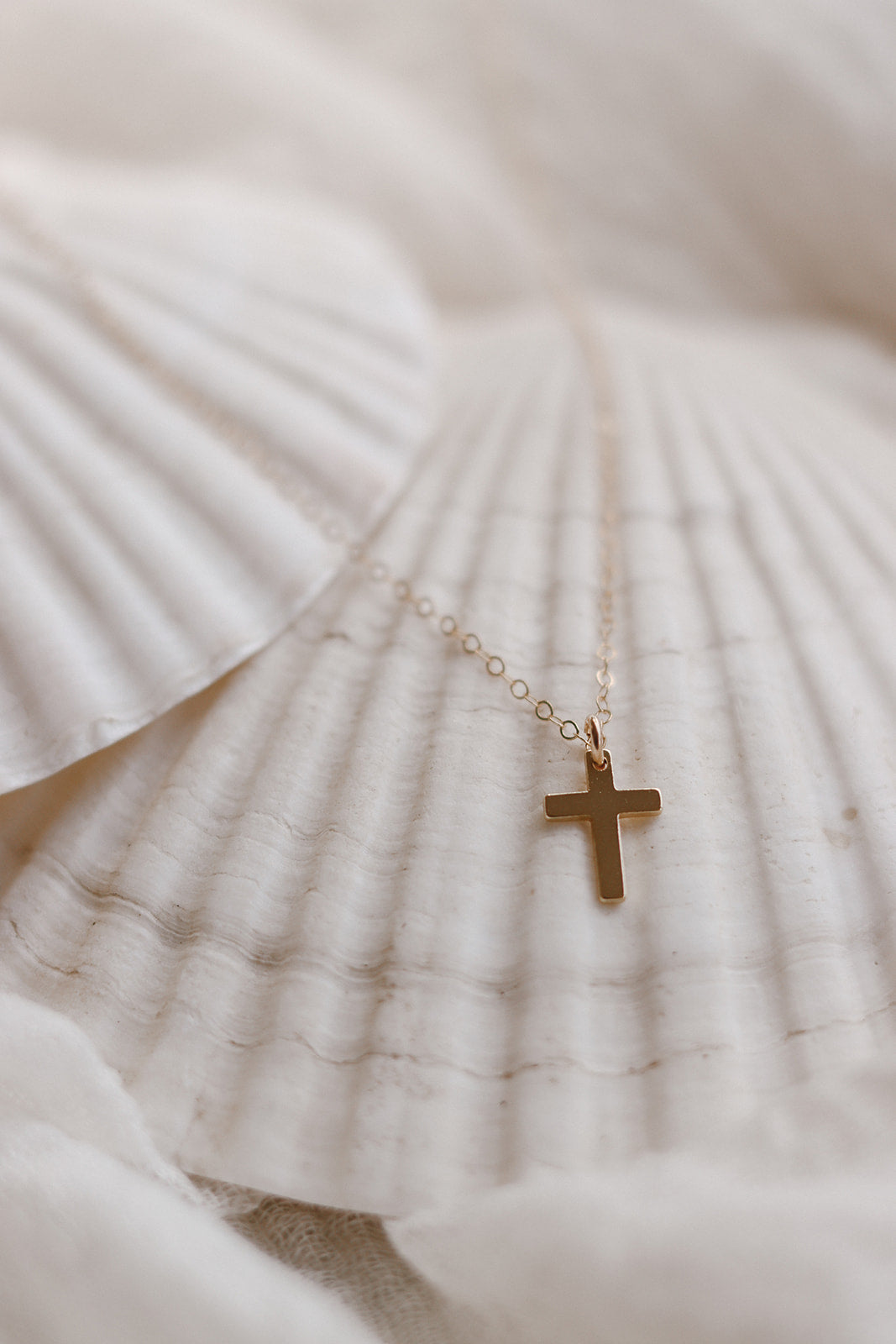 Gold cross pendant necklace on thin chain over white fabric, small cross charm