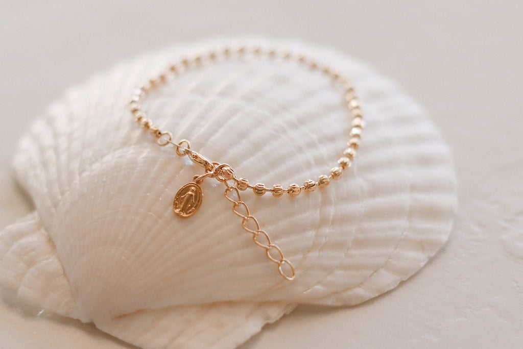 Gold-tone medal bracelet with oval medal charm and dangling chain extender.
