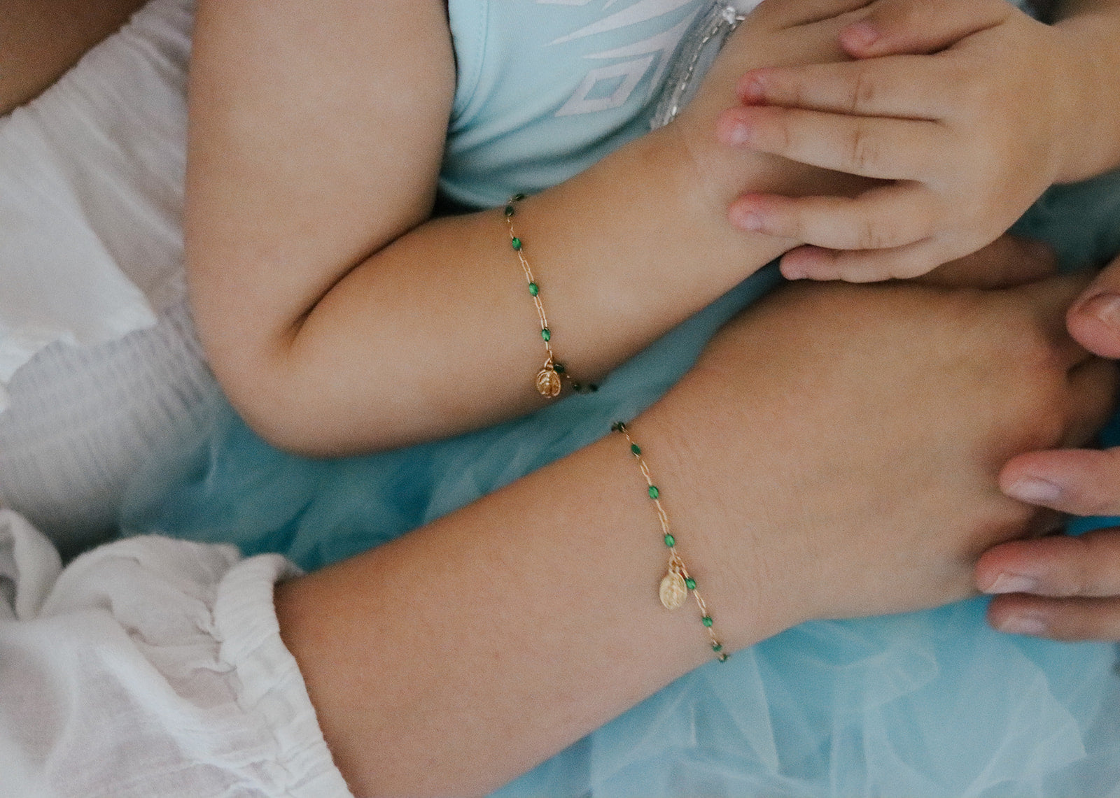 Green beaded bracelet with oval medal charm on wrist, gold-tone links
