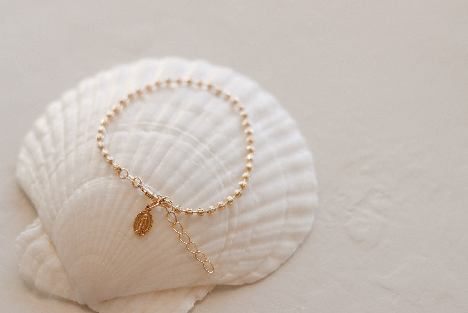 Gold-tone medal bracelet with oval charm and small dangling cross charm