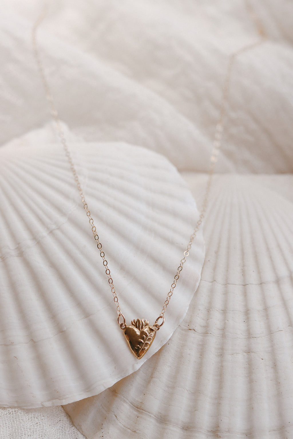 Gold heart pendant necklace on white fabric and seashells, fine chain