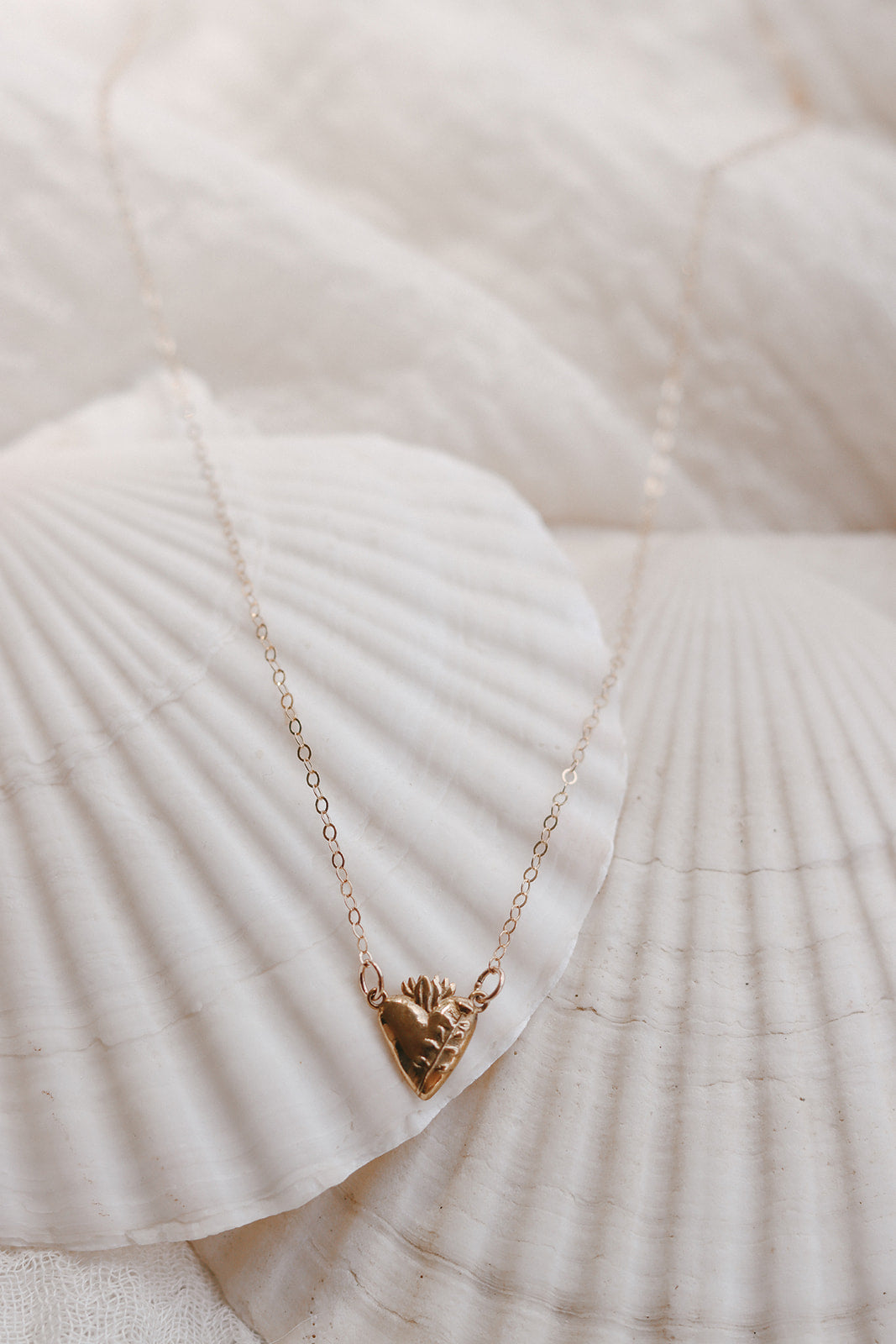 Gold heart pendant necklace on white fabric and seashells, fine chain