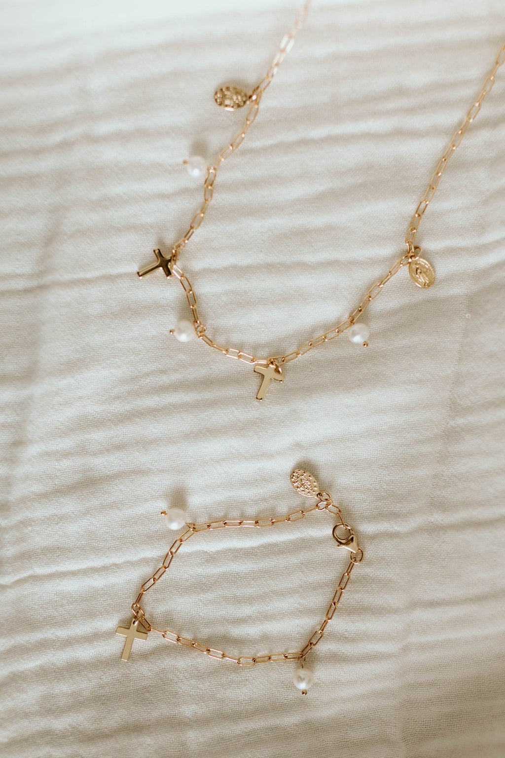 Gold-tone necklace set on light fabric with cross charm and pearl bead accents.
