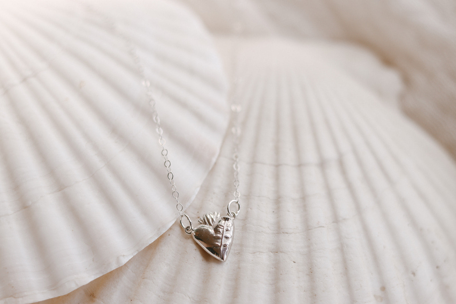 Sterling silver heart pendant necklace on white fabric, heart charm centered on chain