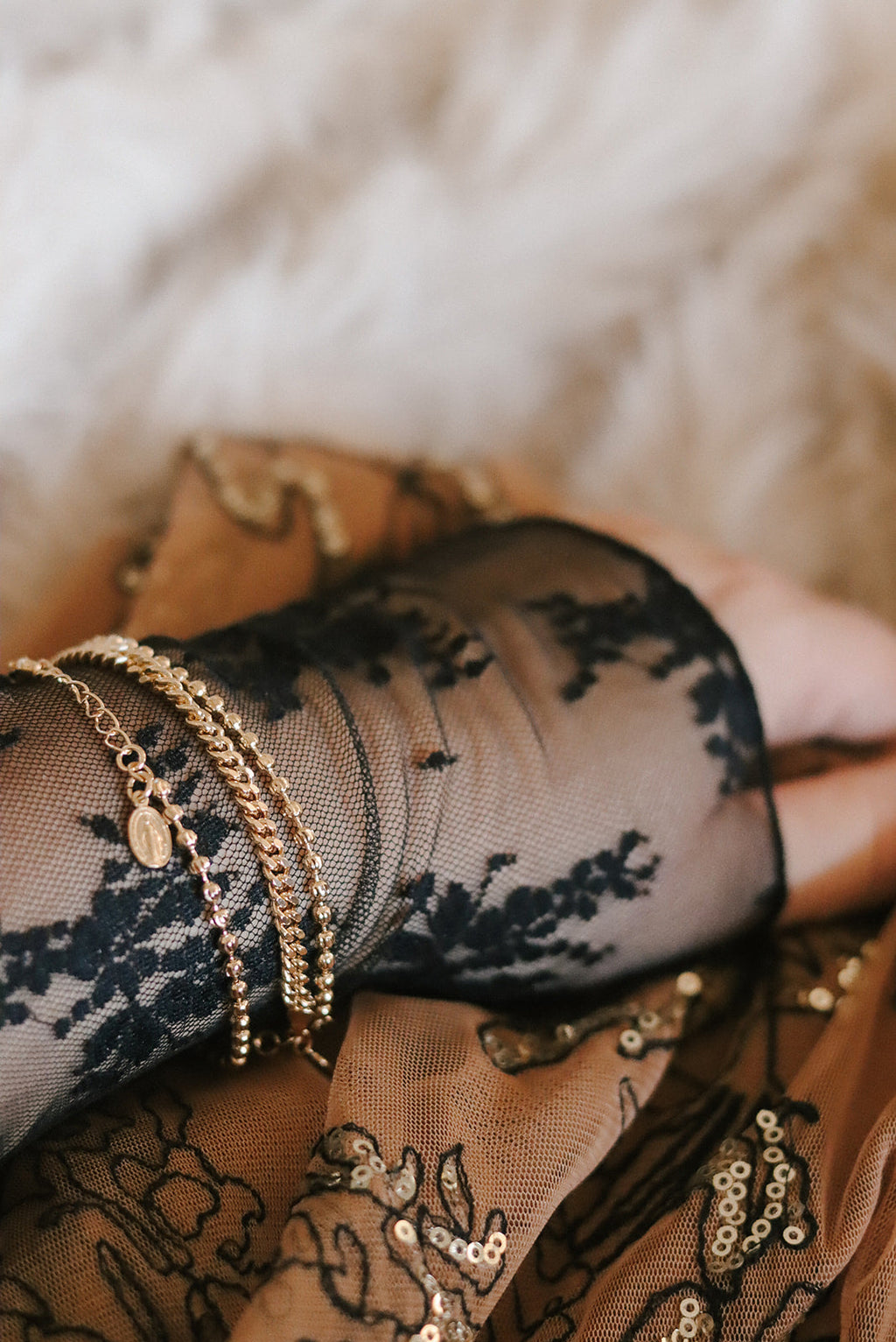 Gold-tone medal bracelet stacked on wrist with multiple chain bands and oval charm.