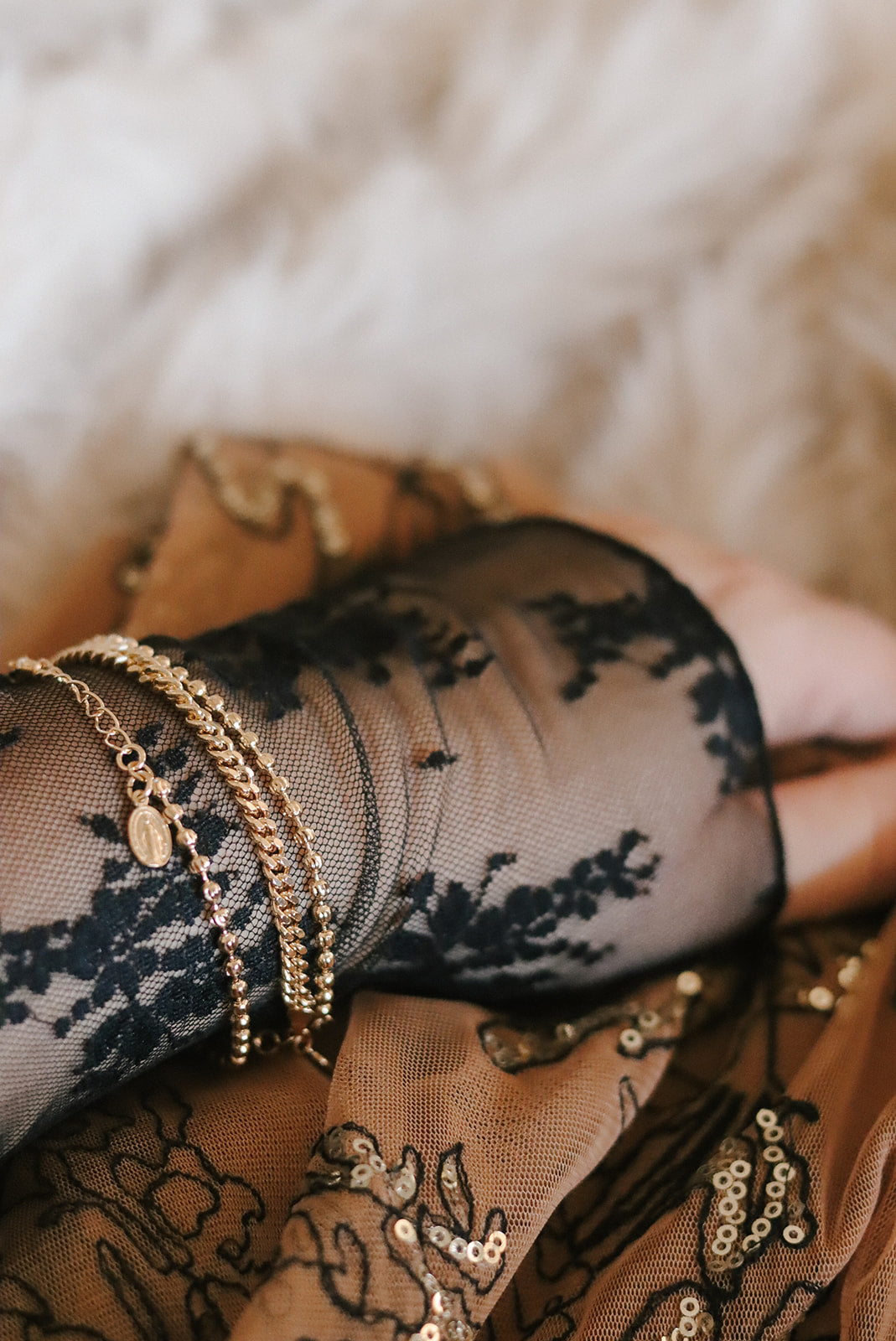 Gold-tone medal bracelet stacked on wrist with multiple chain bands and oval charm.