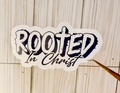 Rooted in Christ vinyl sticker, white background with bold dark text and cross