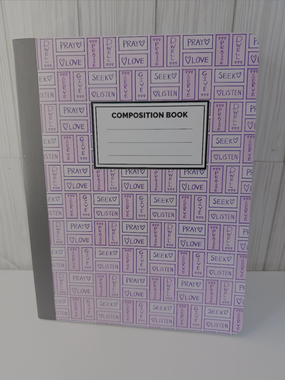 Pink and purple composition book with prayer-themed pattern and ruled writing lines