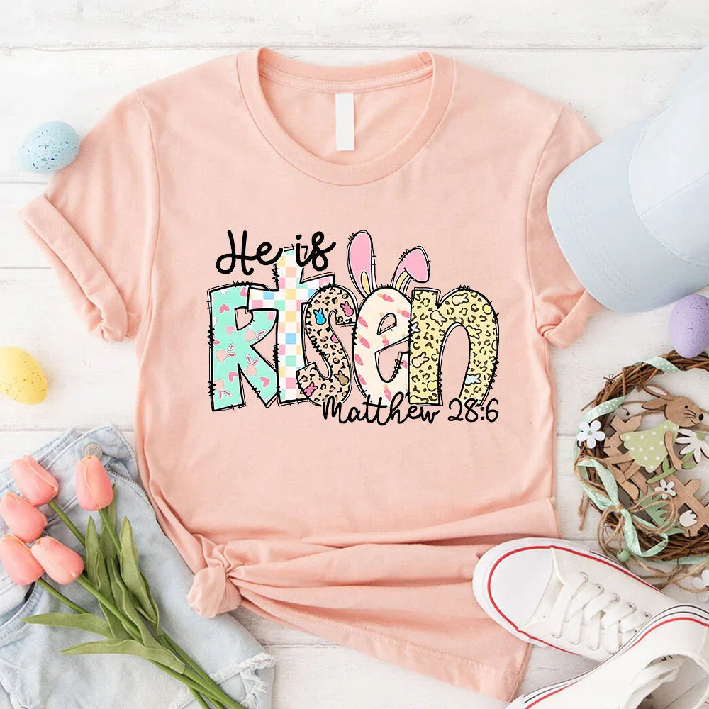 Peach T-shirt with colorful 'He is Risen' bunny graphic and 'Matthew 28:6'.
