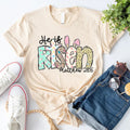 Cream crewneck T-shirt with colorful 'He is Risen' bunny graphic and 'Matthew 28:6' text