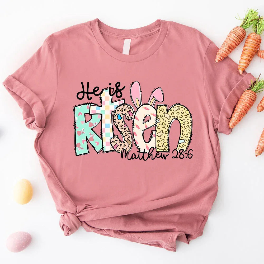 Dusty pink T-shirt with colorful 'He is Risen' bunny graphic and 'Matthew 28:6'.