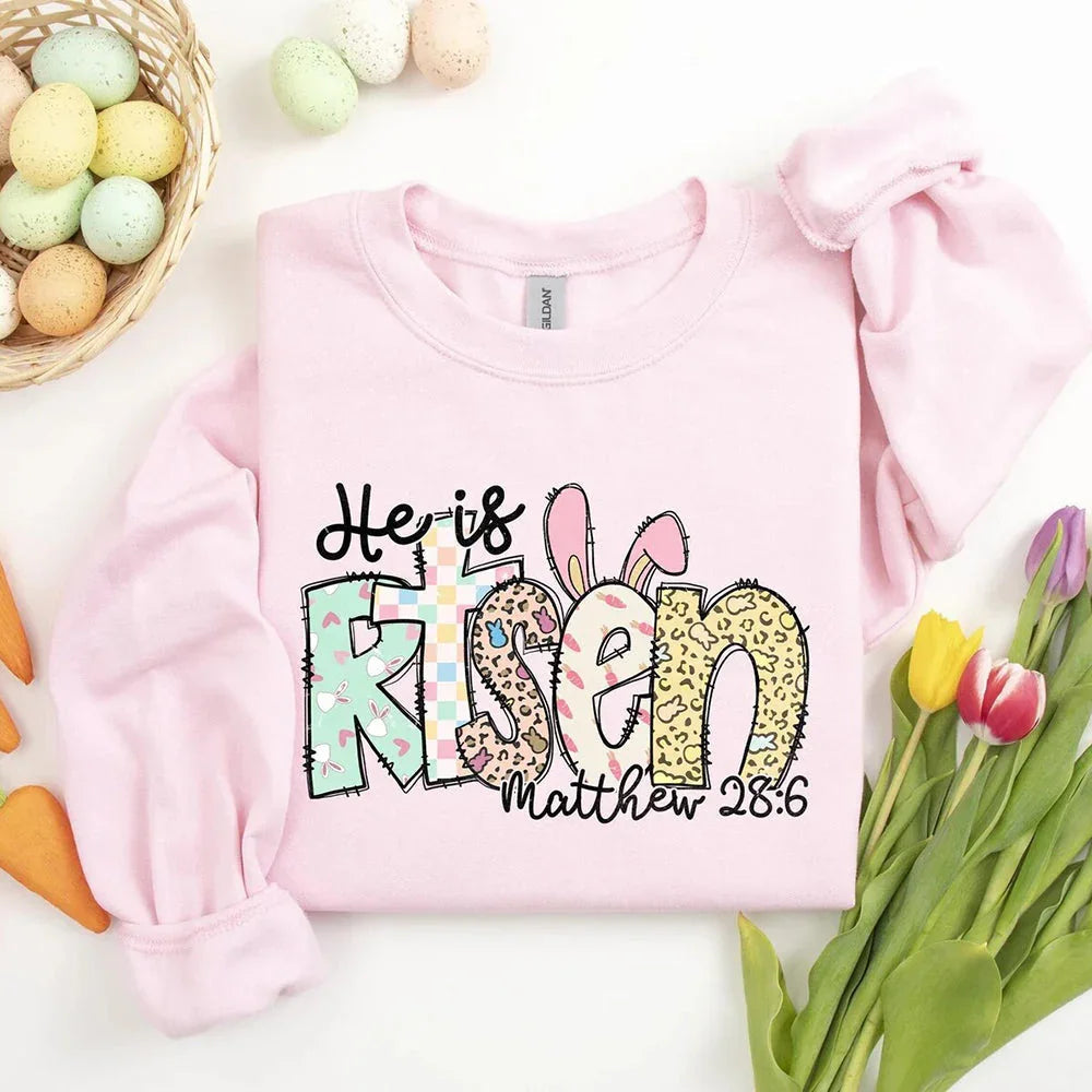 Light pink crewneck T-shirt with colorful 'He is Risen' bunny graphic and 'Matthew 28:6' text