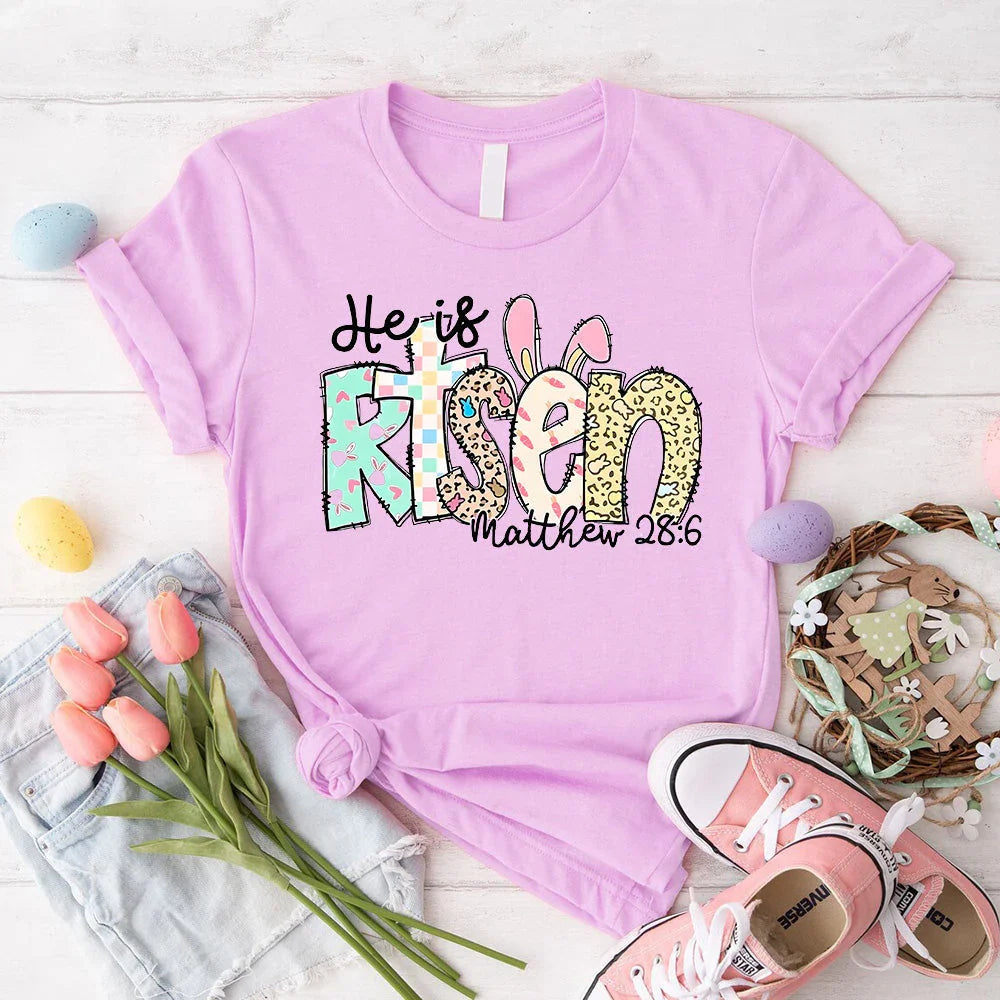 Lilac T-shirt with colorful 'He is Risen' bunny graphic and 'Matthew 28:6'.