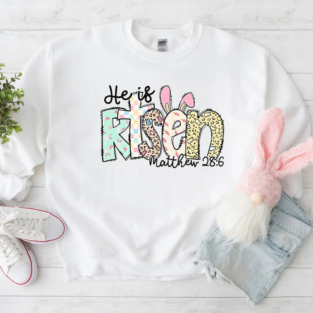 White crewneck T-shirt with colorful 'He is Risen' bunny graphic and 'Matthew 28:6' text