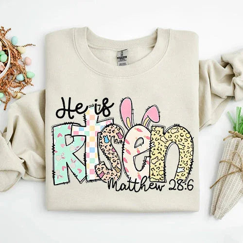 Light cream short-sleeve T-shirt with colorful 'He is Risen' bunny graphic and 'Matthew 28:6'