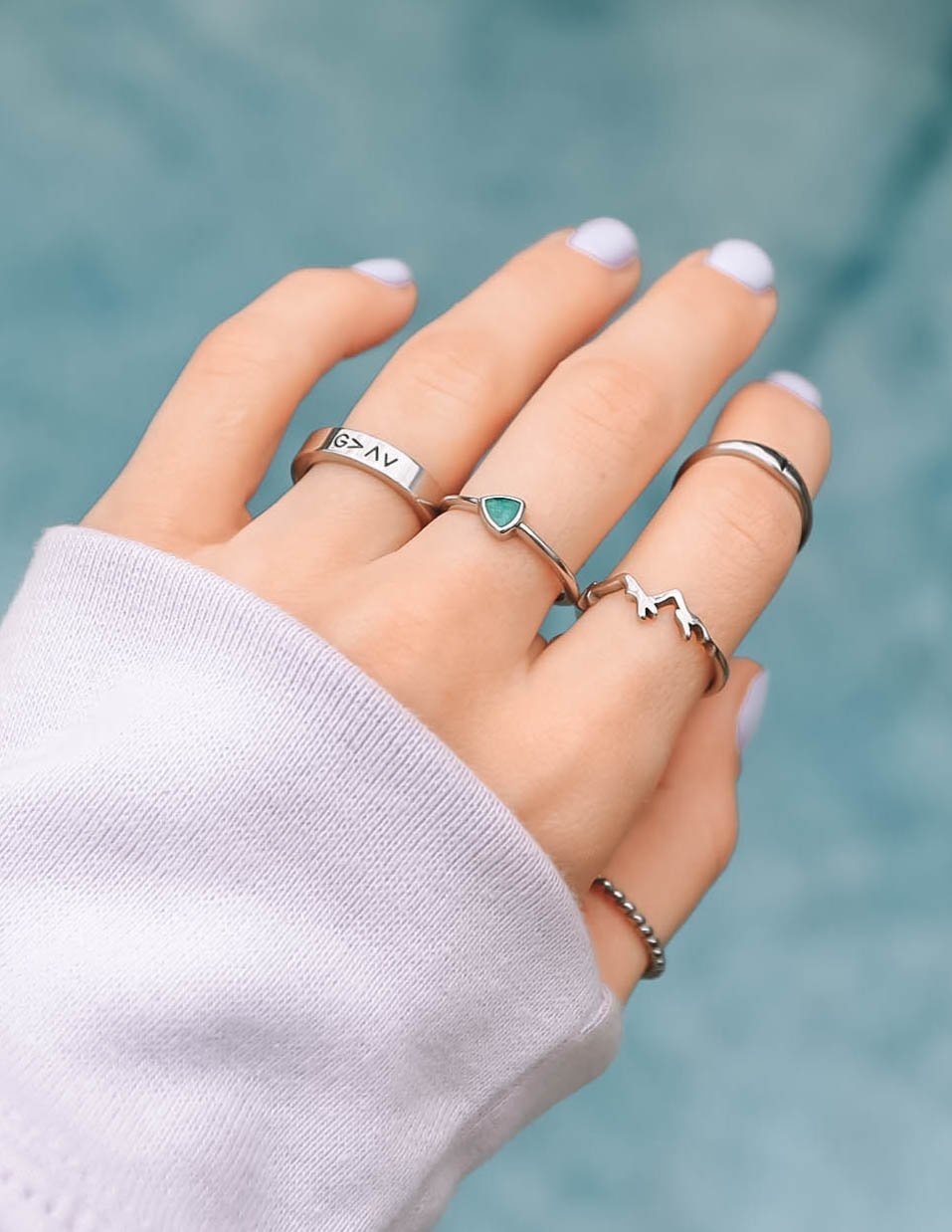 Silver mountain ring on hand, stacked with other rings and green stone band.
