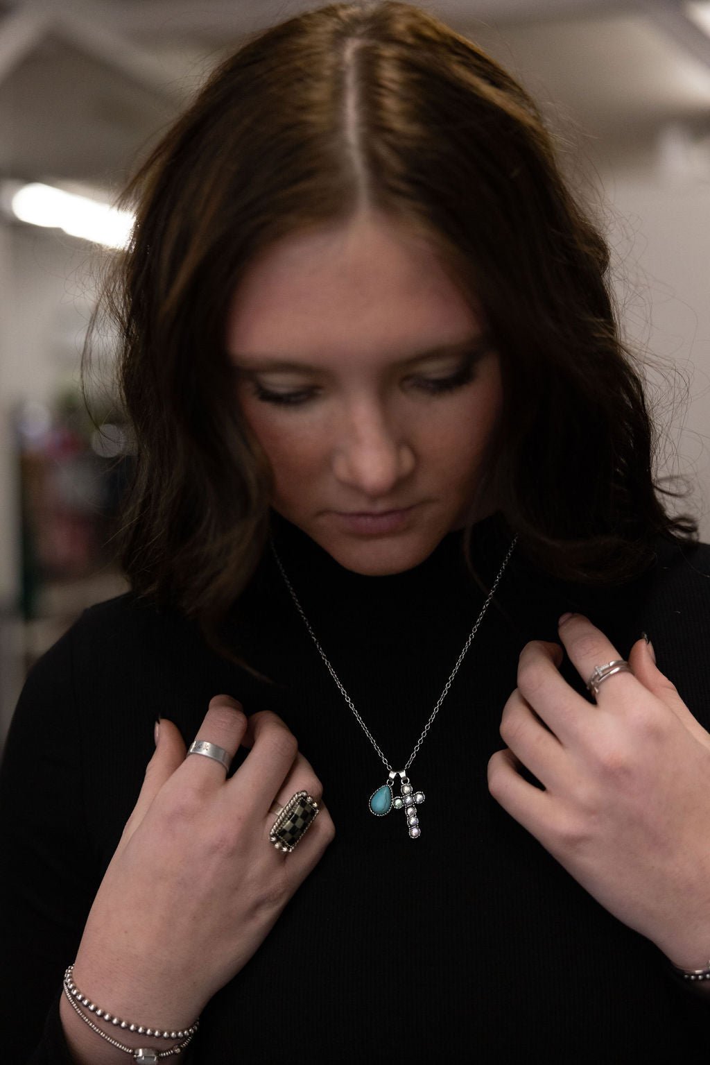 Turquoise teardrop cross necklace on silver chain, close-up while worn by model