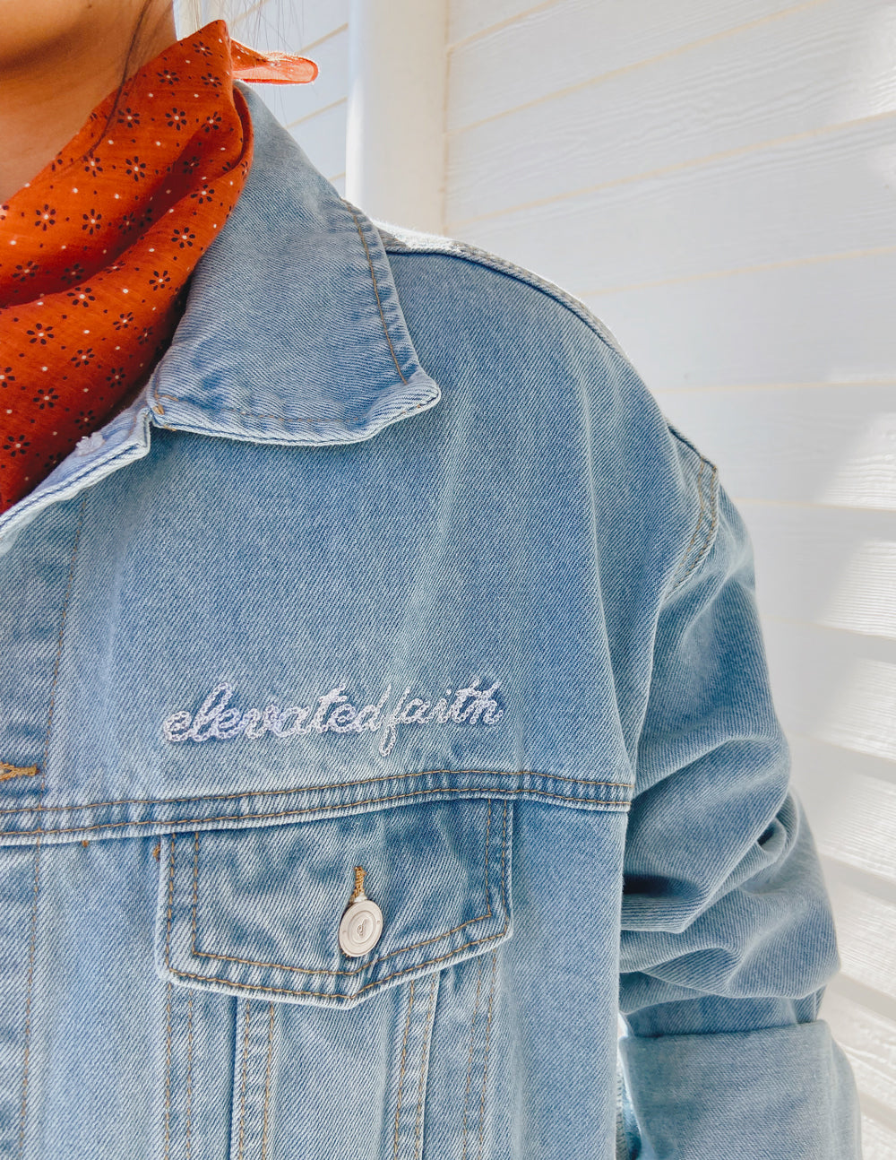 Light-wash denim jacket collar and shoulder seam with embroidered text