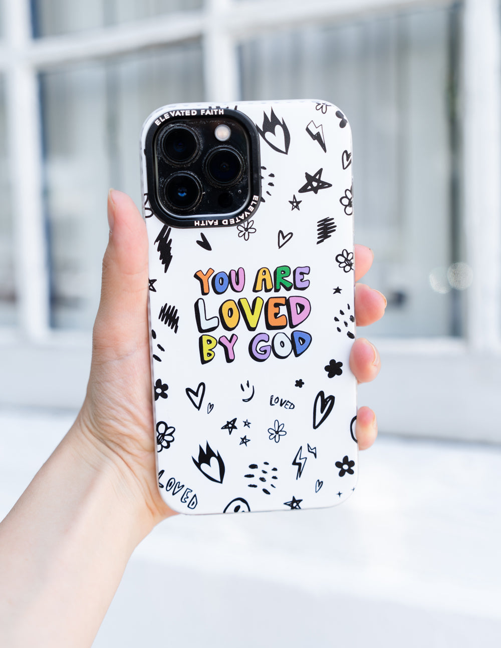 White phone case with 'You are loved by God' text and black icon pattern, held
