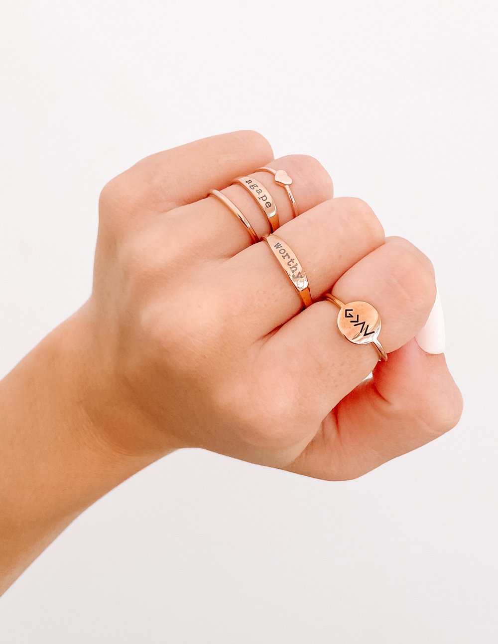 Rose gold stack of rings on fingers with engraved bands and small charm