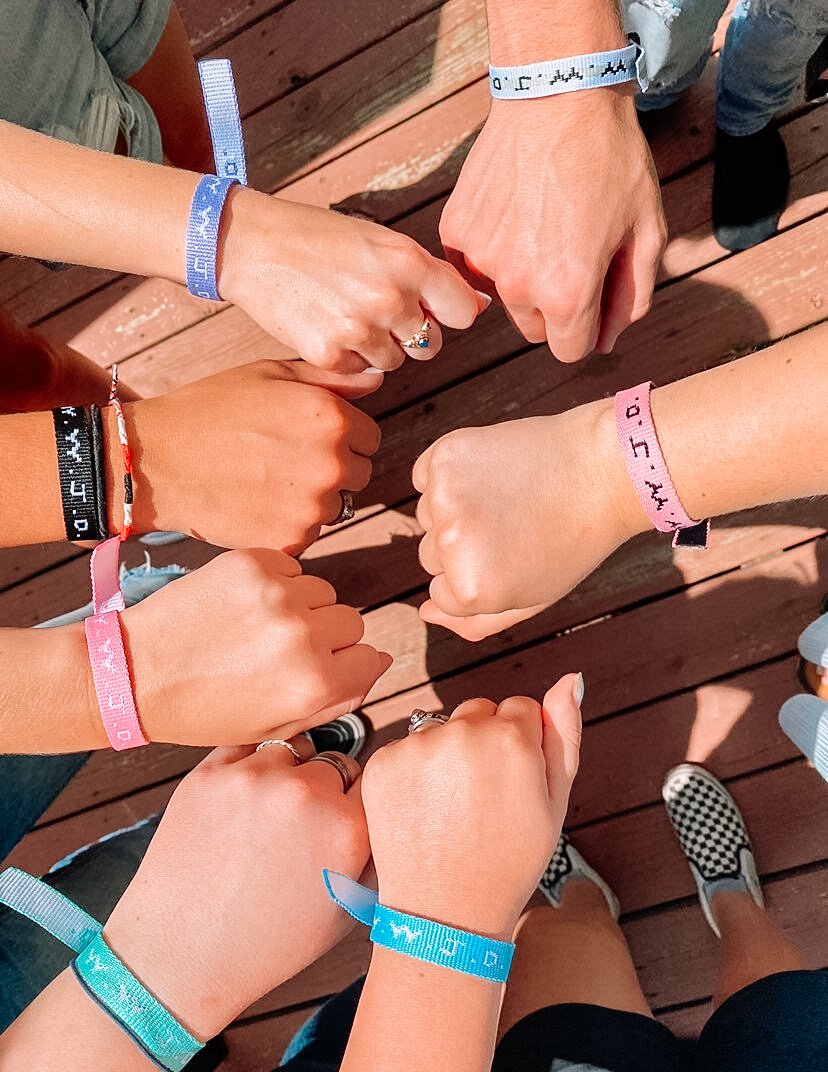 Set of colorful woven WWJD-style friendship bracelets being fastened by hands