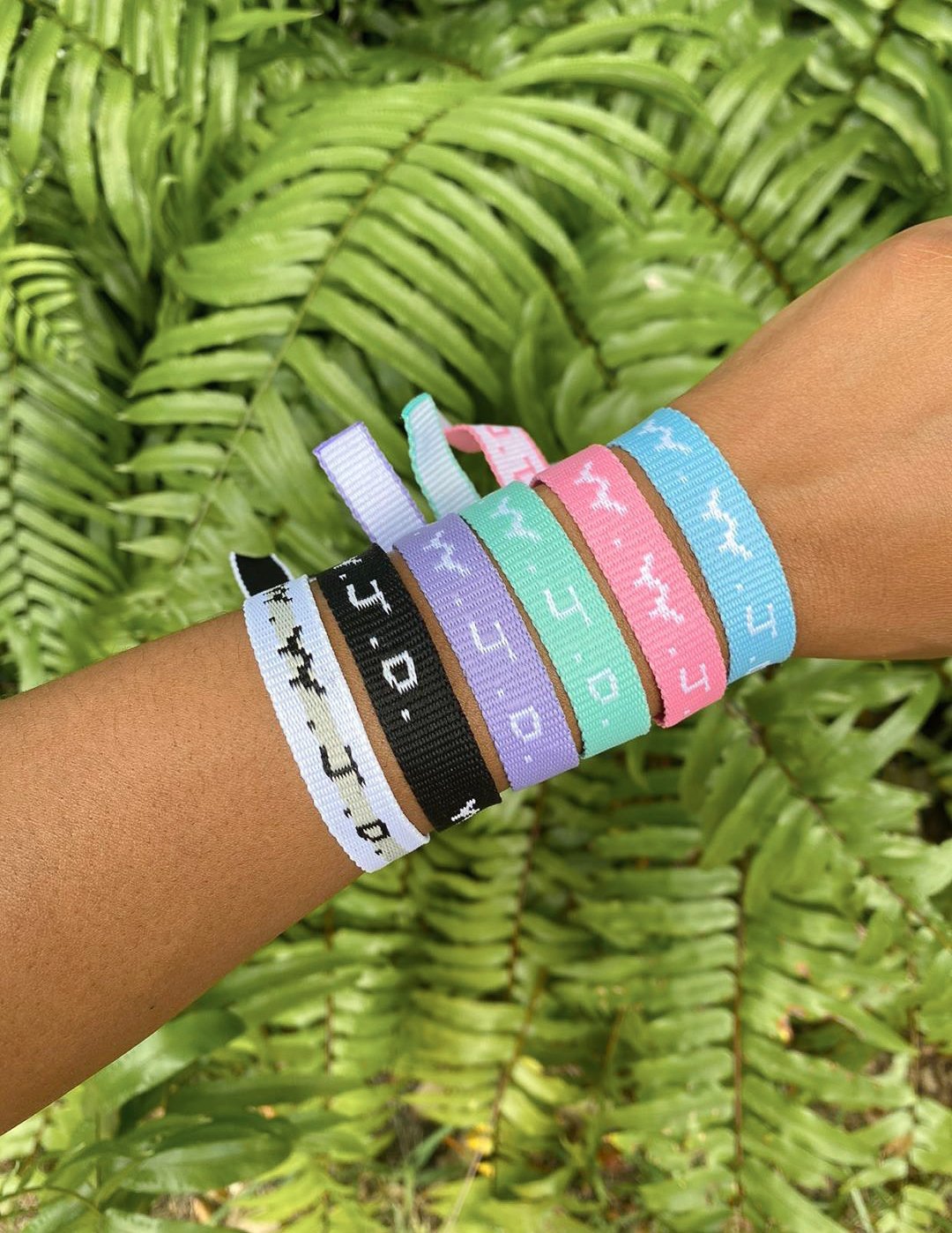 Colorful woven WWJD-style friendship bracelets in pastel tones on a wrist