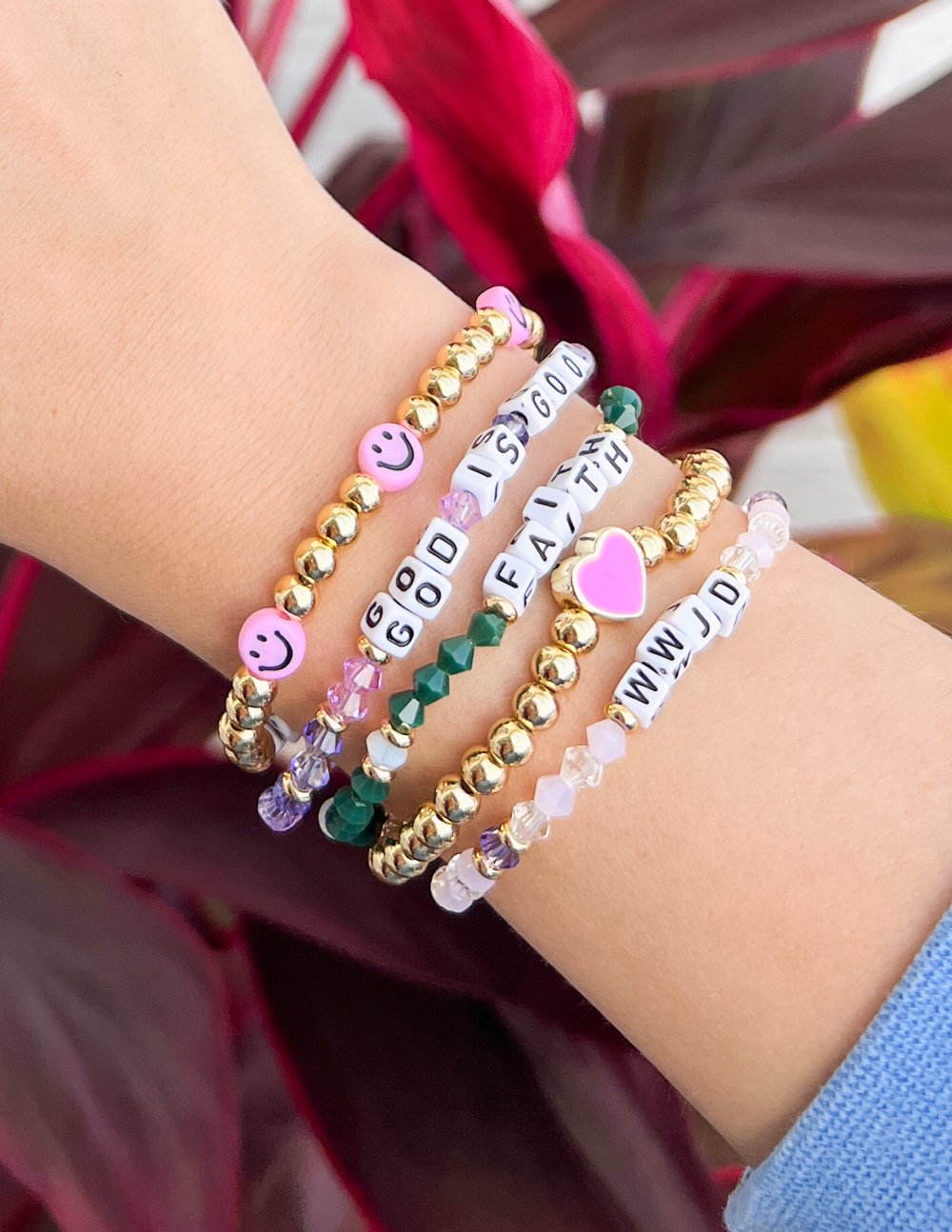 WWJD letter bracelets on wrist with gold beads, colorful stones, and smiley letter charms