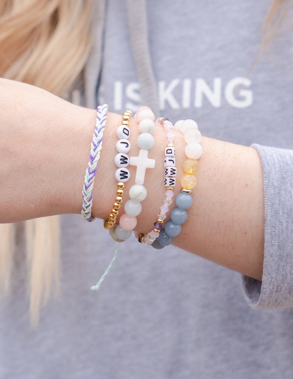 WWJD letter bracelets on wrist with white and pastel beads, gold details, and letter blocks