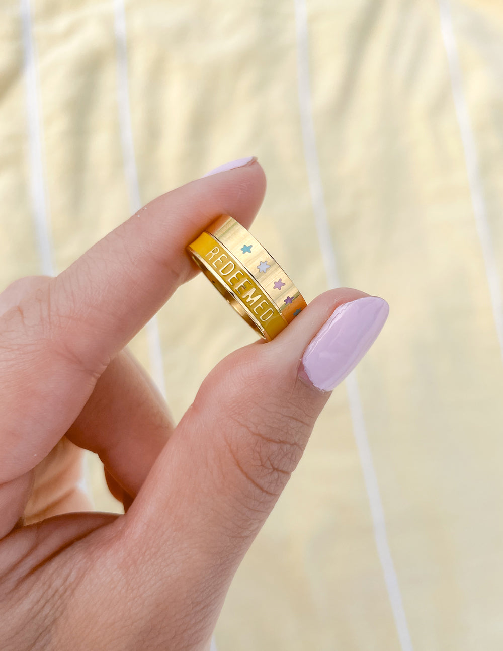 Gold-tone yellow enamel ring held in hand, REDEEMED text visible